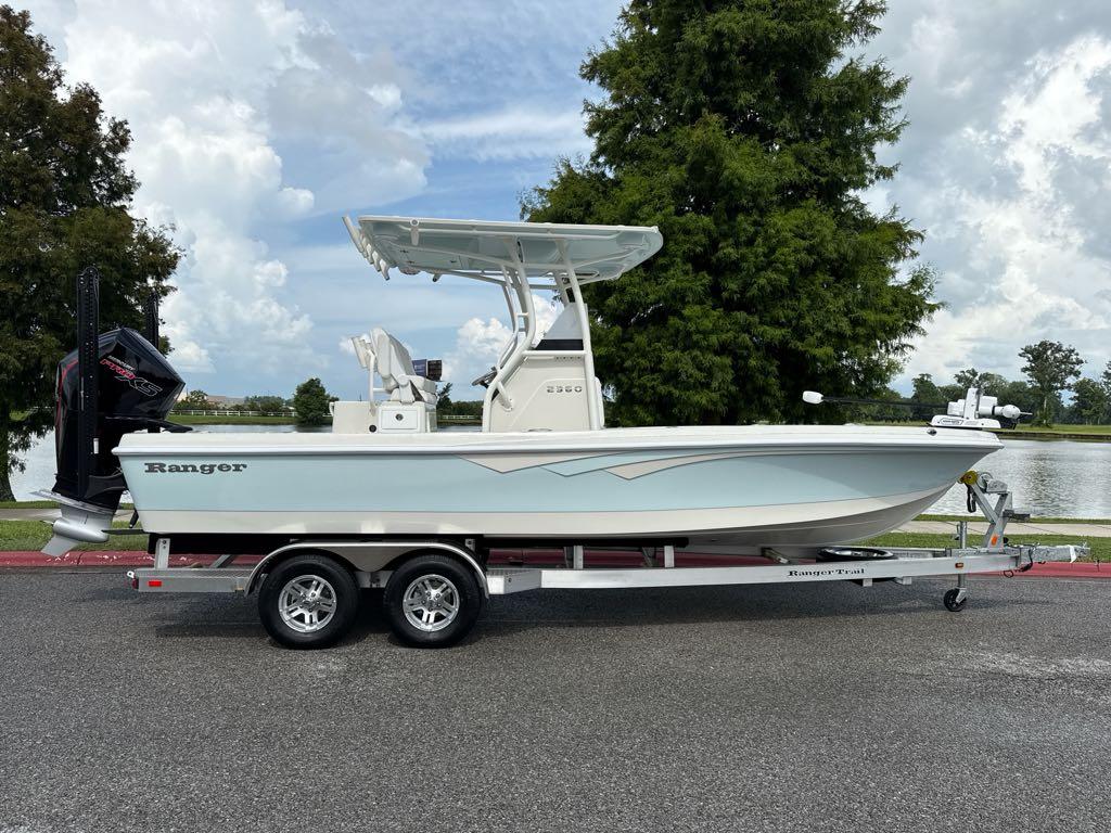 2025 Ranger 2360 Bay boat on trailer, parked near a lake with trees in background.