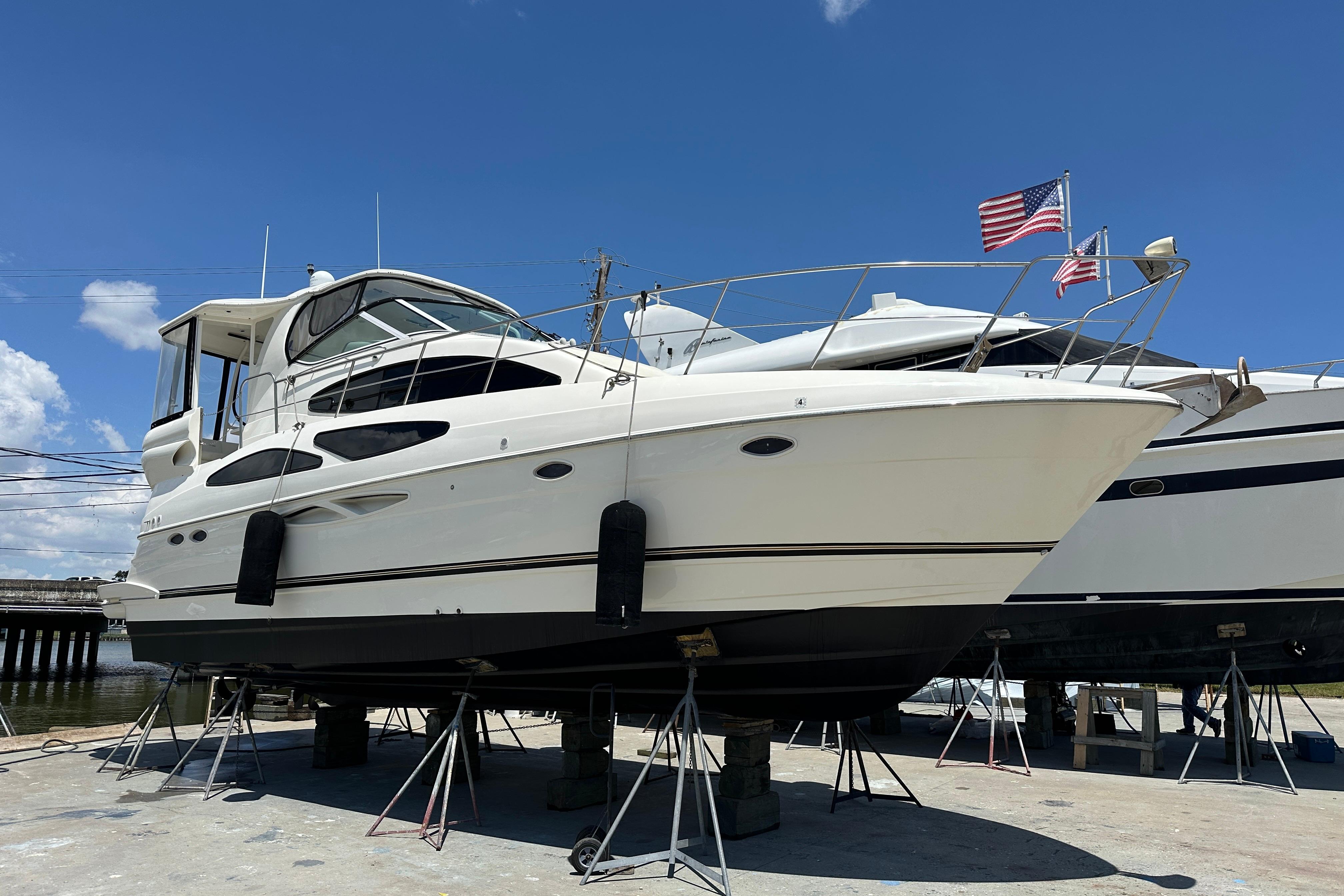 2004 Cruisers Yachts 405 Express Motoryacht on stands, with American flag, under clear blue sky.