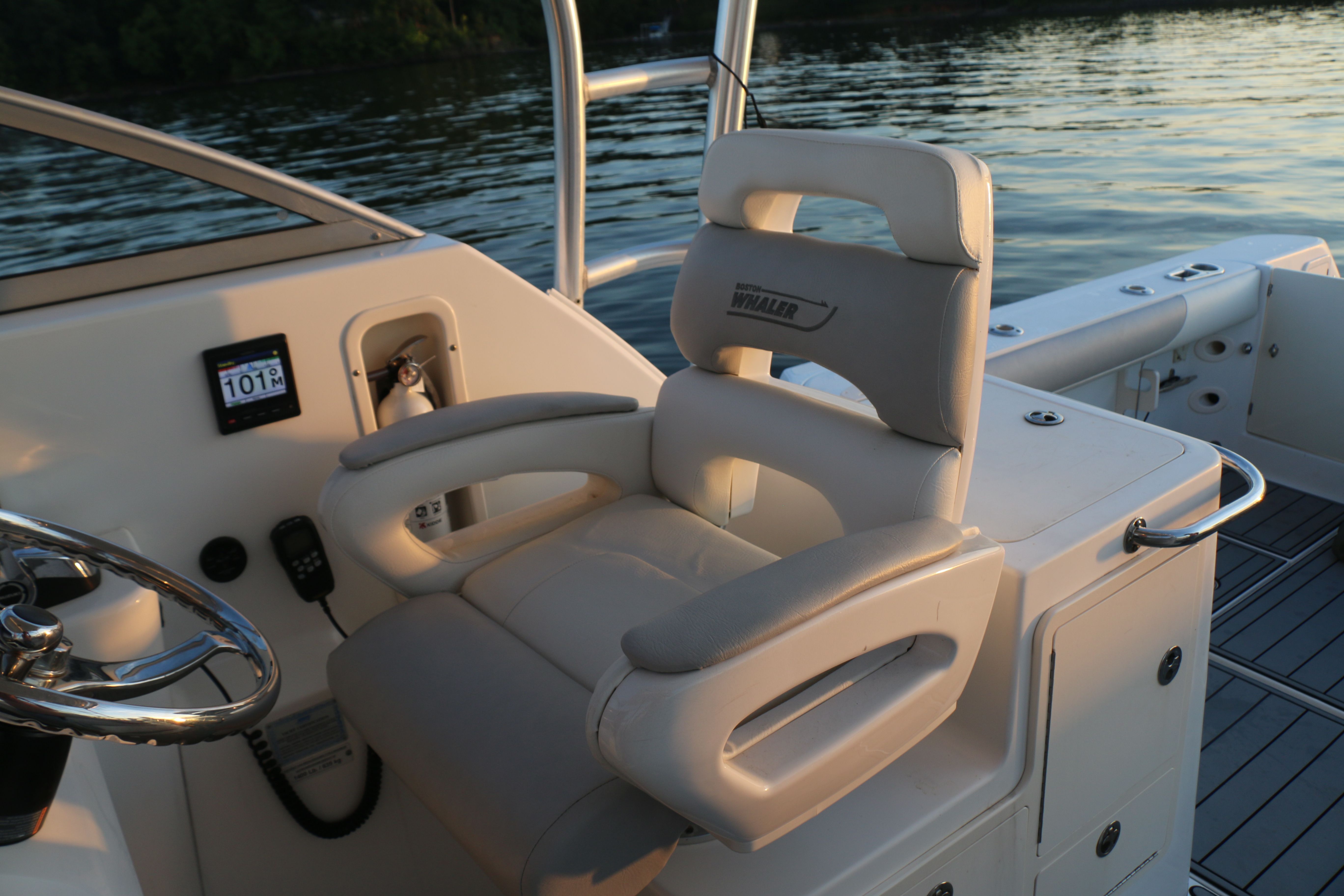 A helm station with a cushioned seat on a boat, surrounded by water at sunset.