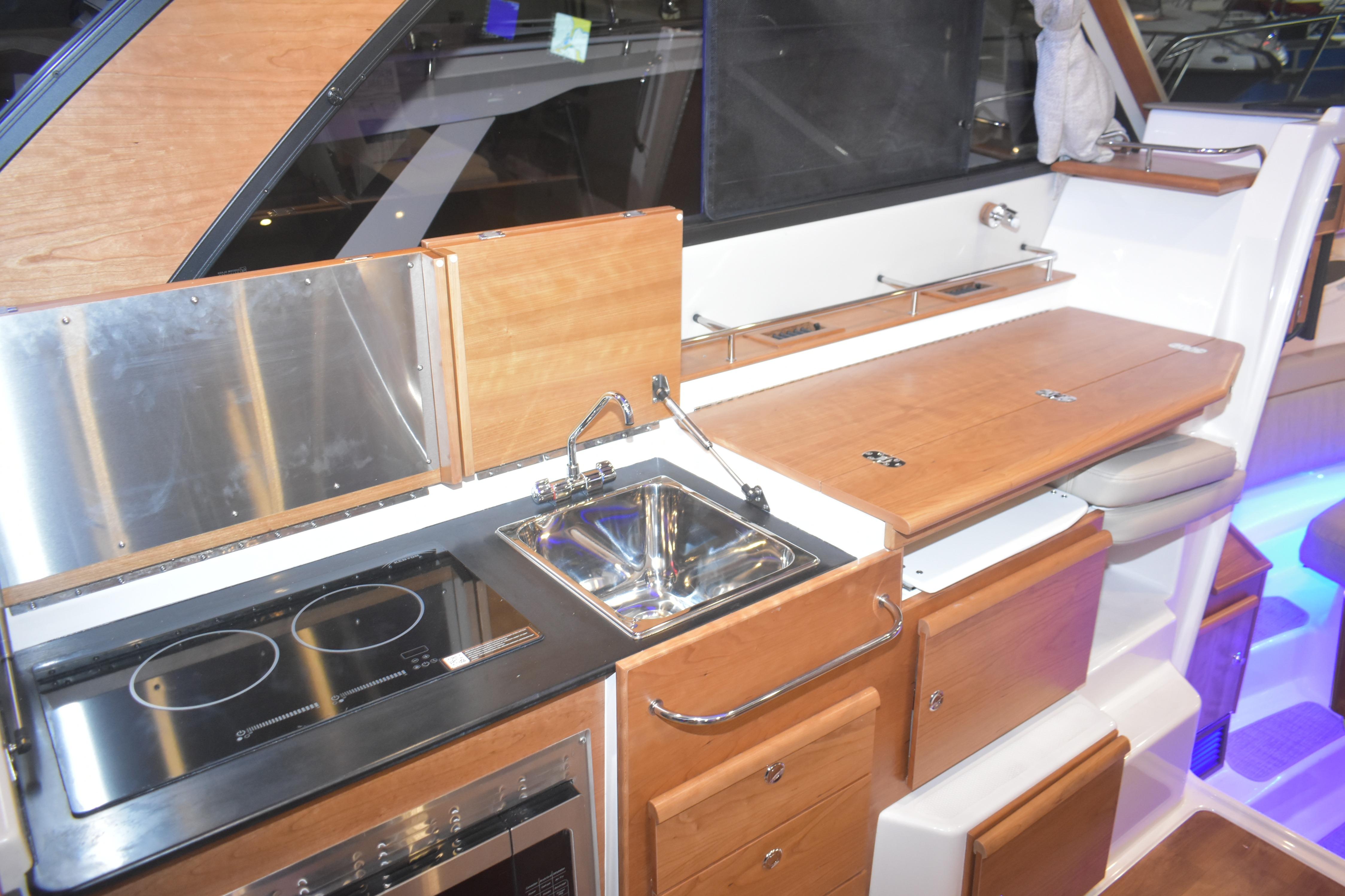 2026 Cutwater C-32 CB yacht kitchen with stove, sink, and wooden cabinetry.
