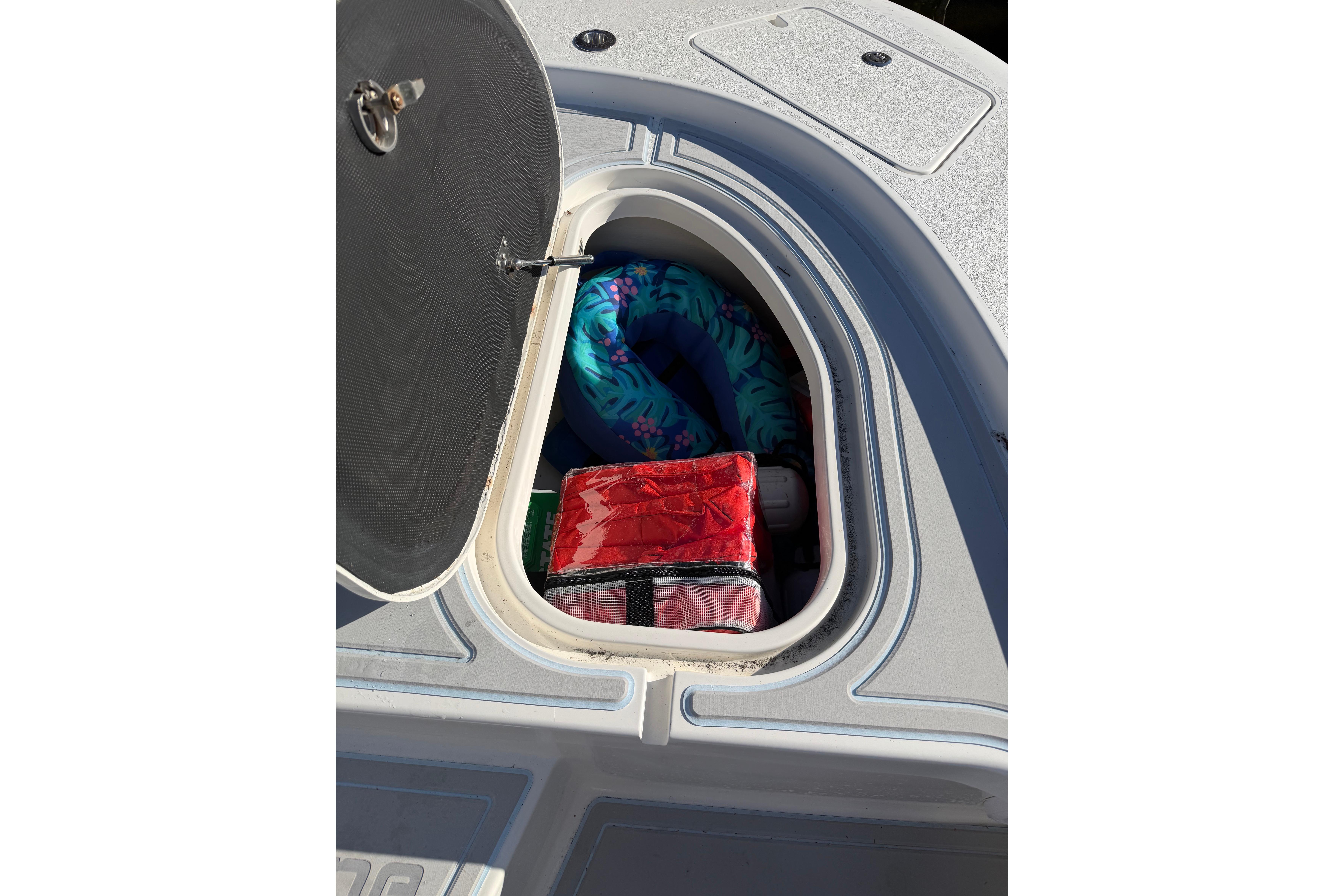 Open storage compartment on 2020 Tideline 235 Hybrid boat with colorful items inside.