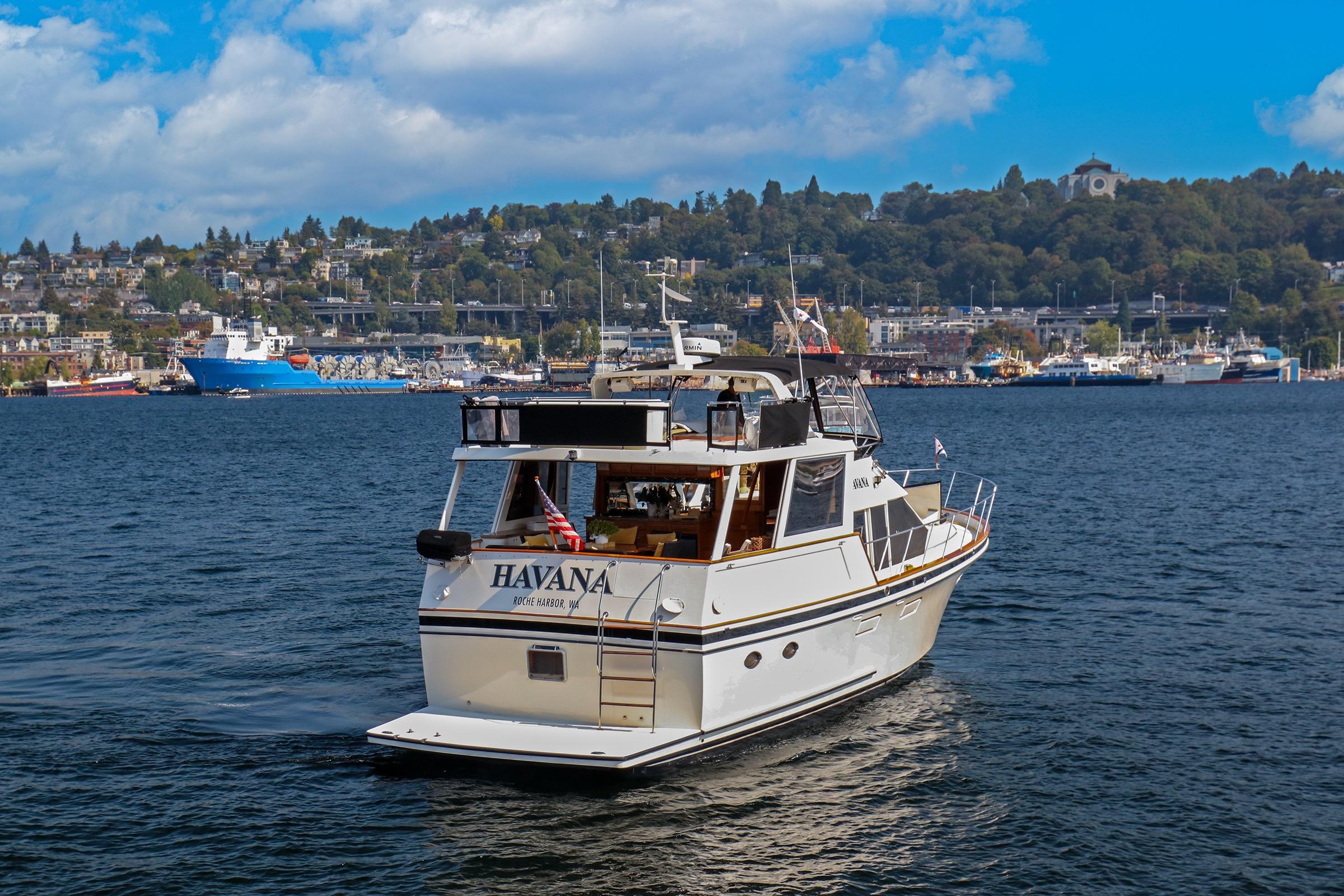 1987 Ocean Alexander 480 Sport Sedan yacht cruising in scenic harbor with cityscape backdrop.