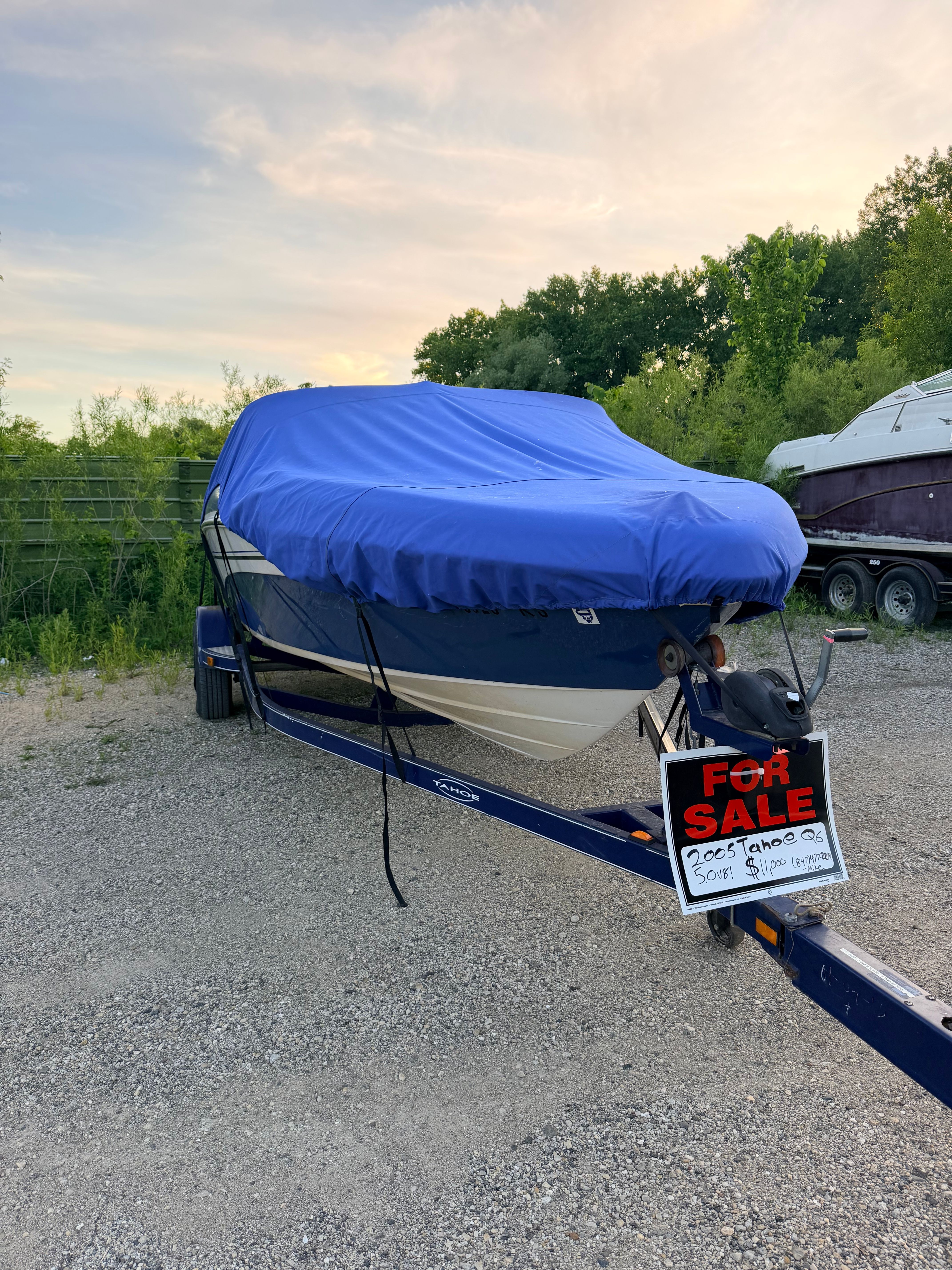 A 2005 Tahoe Q6 Sport boat on a trailer, covered with a blue tarp and a 'For Sale' sign.