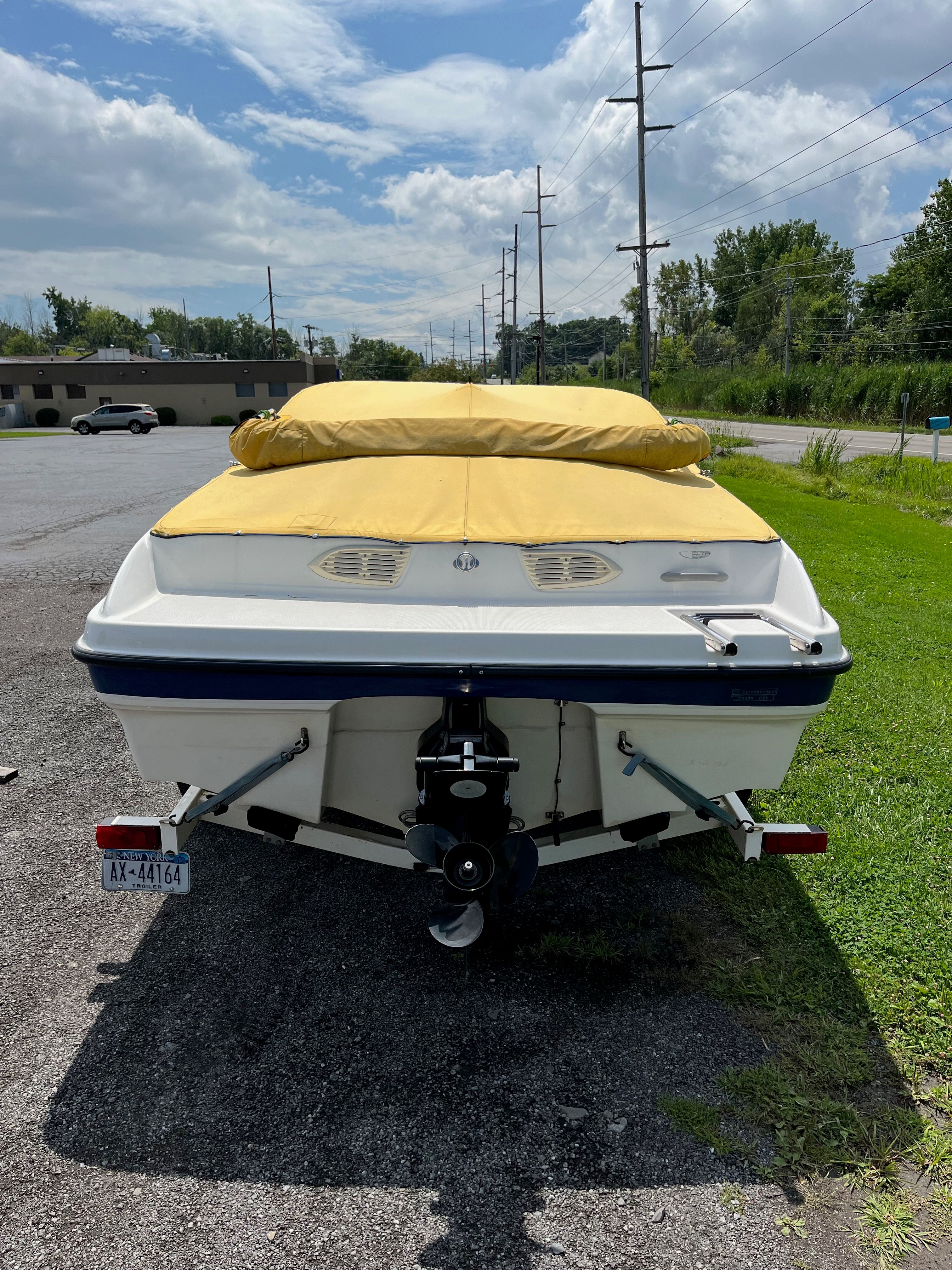 Bayliner 205BR 2005 with a yellow cover on a trailer, parked in a lot.