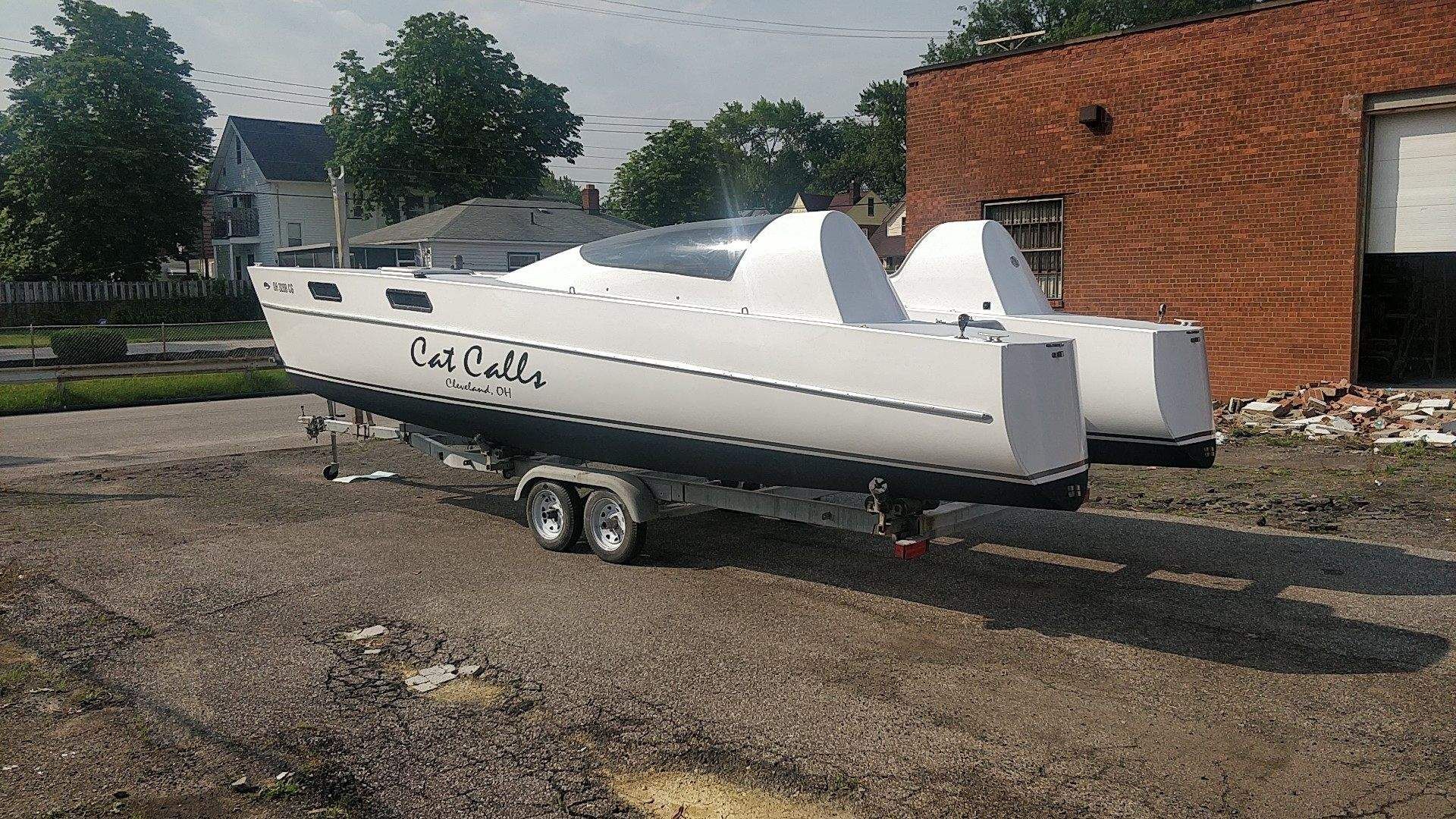 A white catamaran named "Cat Calls" is on a trailer in an urban area.