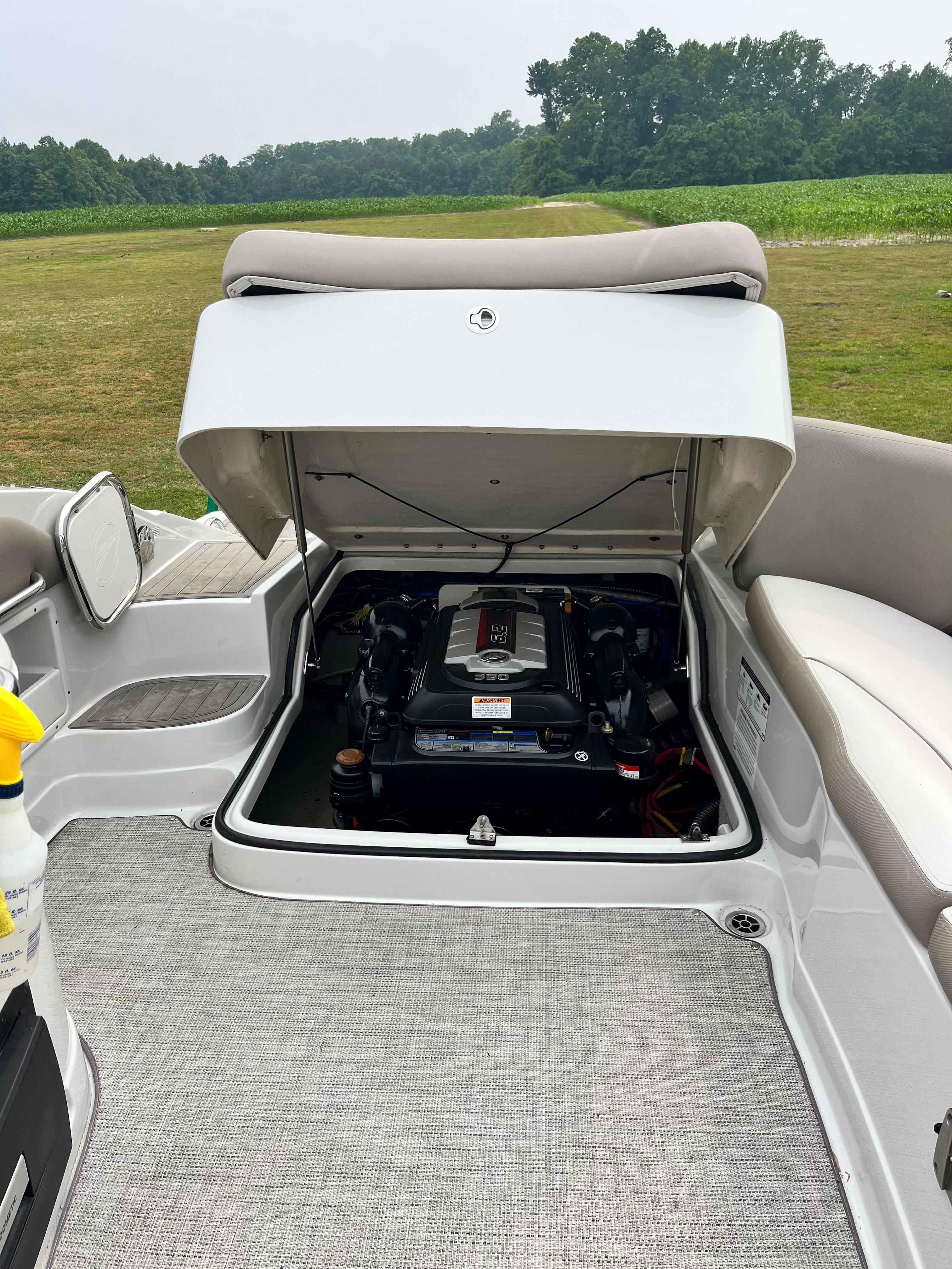 The 2019 Crownline E 285 displays its engine compartment with a well-maintained engine. A green landscape is visible in the background.
