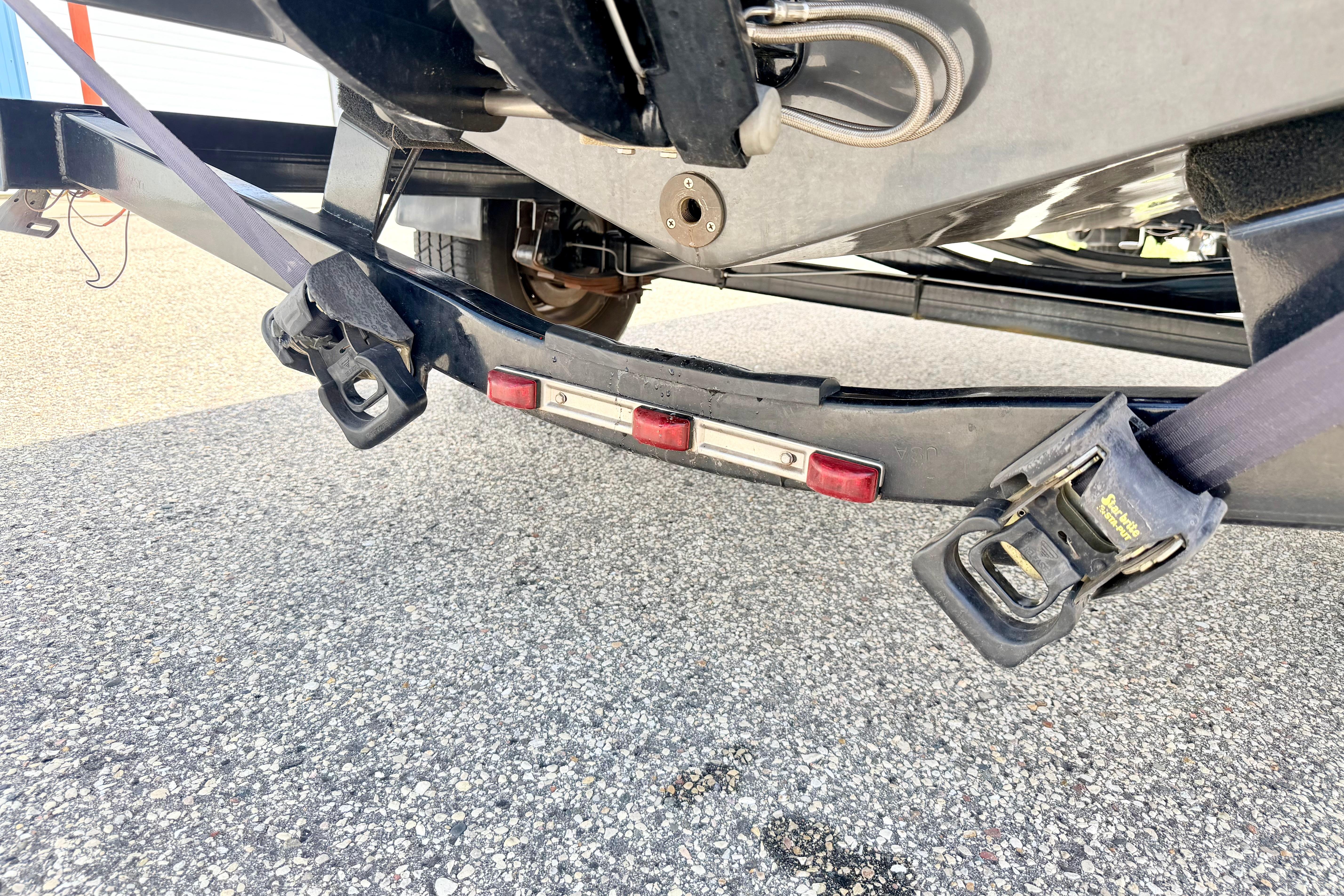 Trailer hitch and straps securing a 2018 Glastron GT 185 boat on pavement.