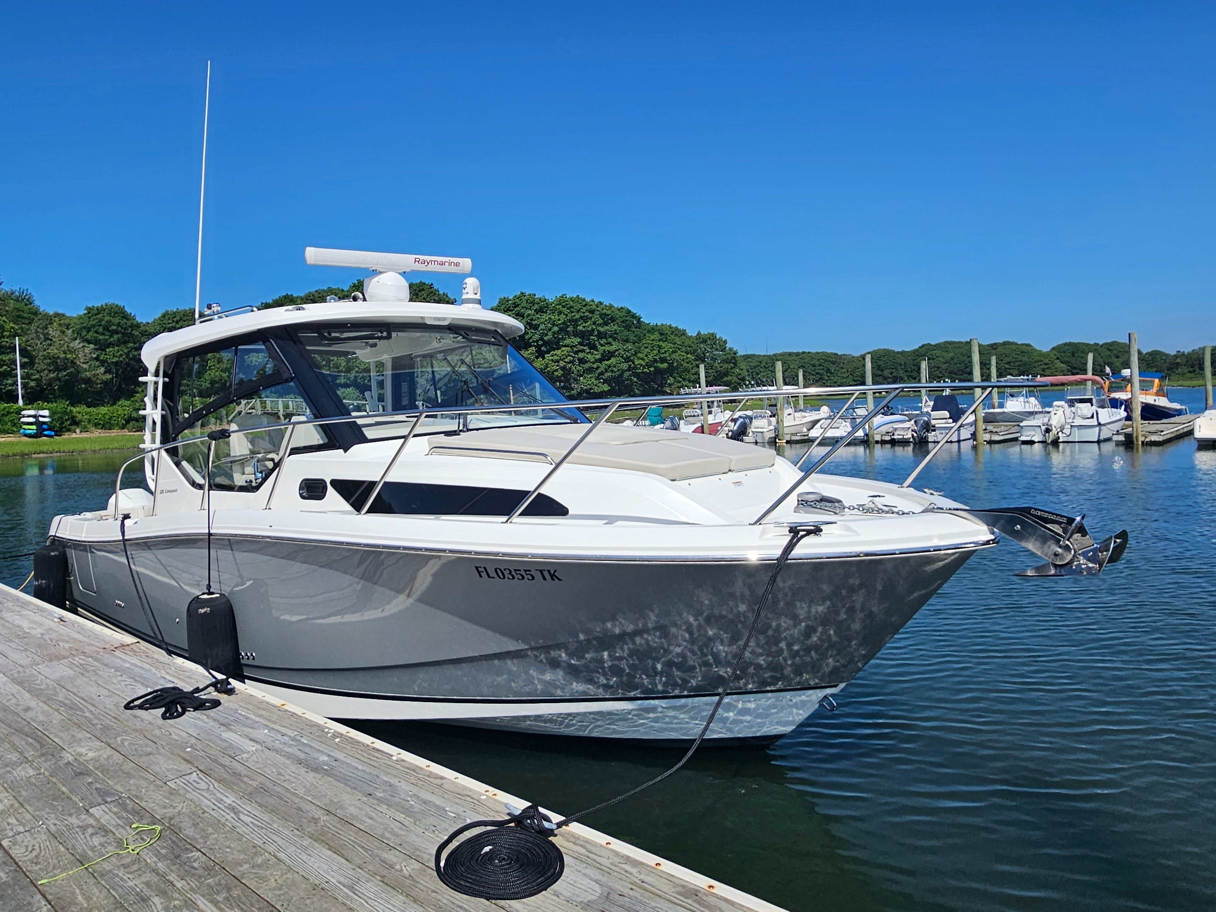 A 2023 Boston Whaler 325 Conquest docked at a wooden pier in a calm harbor.