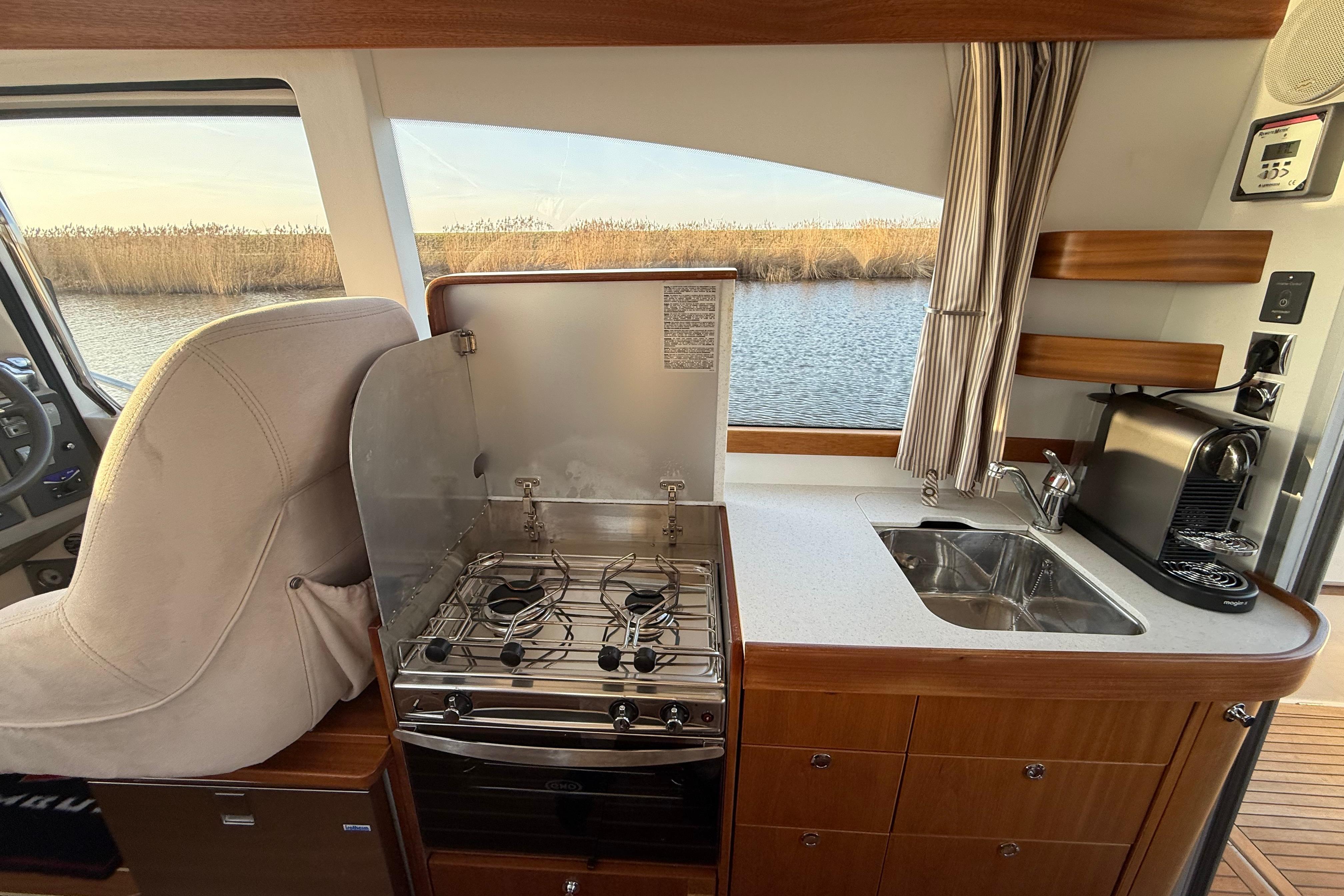 Compact kitchen in 2011 Nimbus 335 Coupe with stove, sink, and coffee maker by a window.