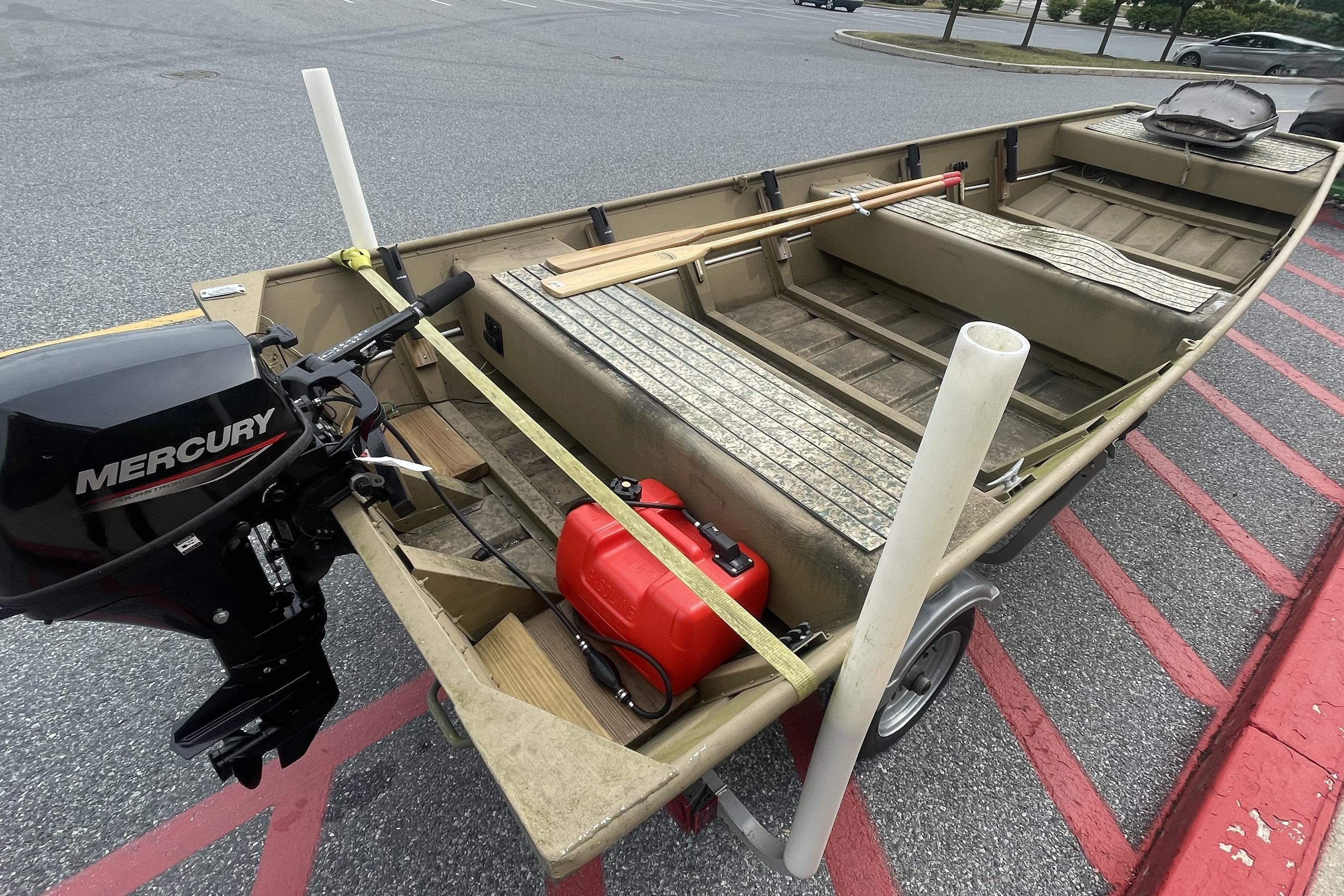 1986 Landau 1664 Jon boat with Mercury motor and red fuel tank in parking lot.