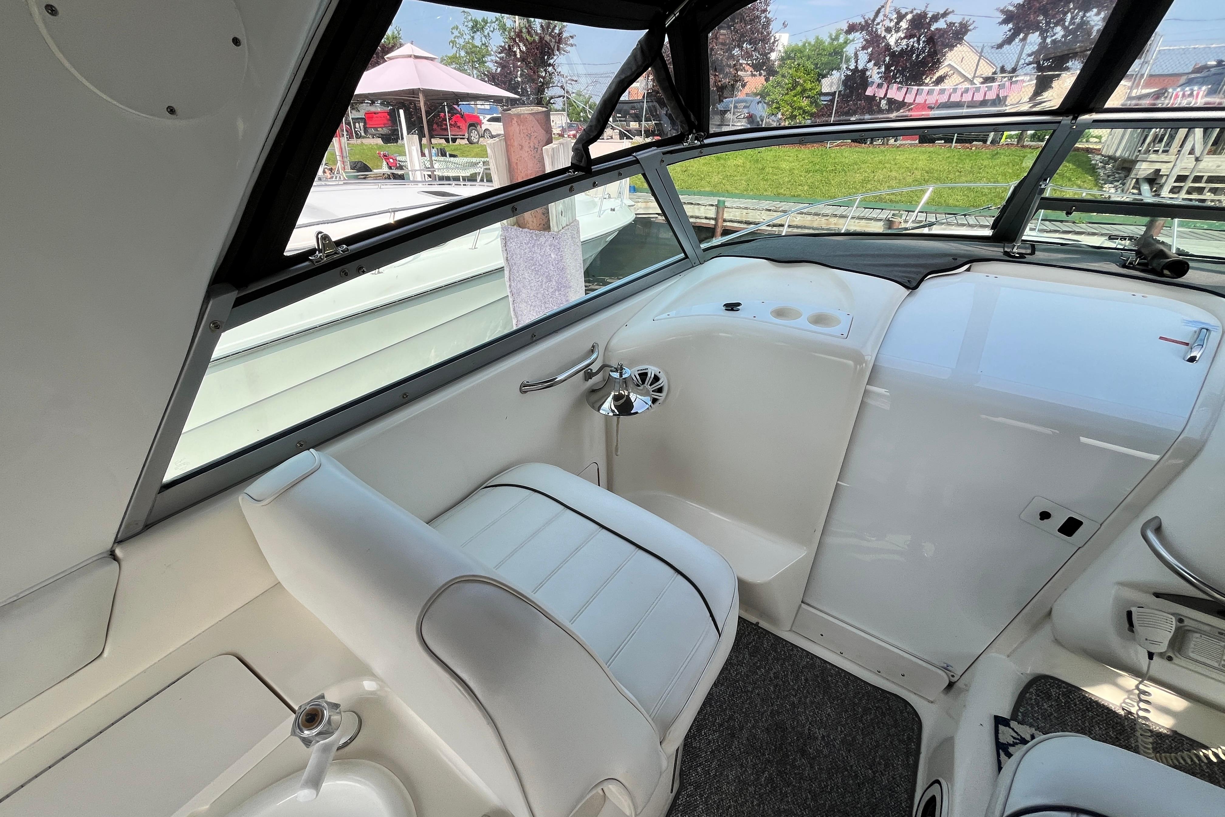 1995 Sea Ray Sundancer 330 cockpit with white seating and dashboard, docked near a garden.