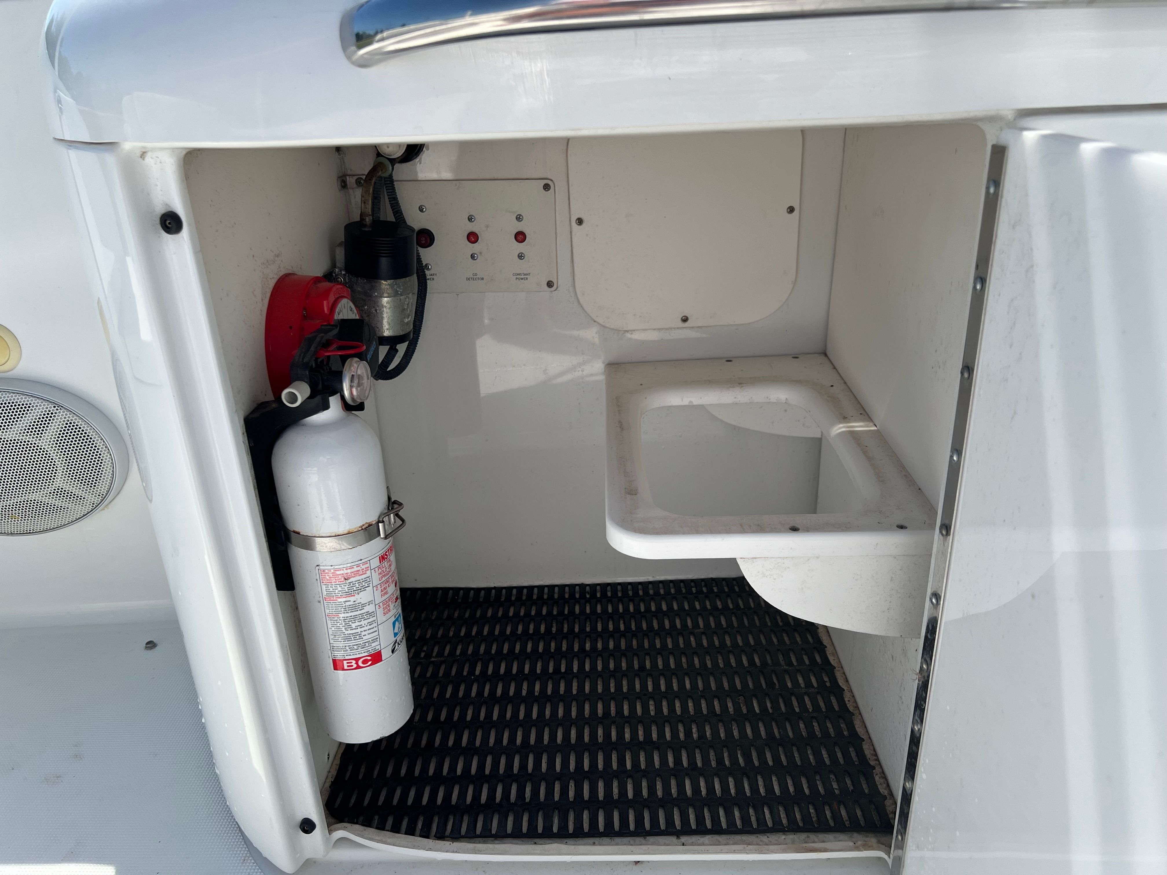 An open storage compartment on a boat with a fire extinguisher and a small sink.