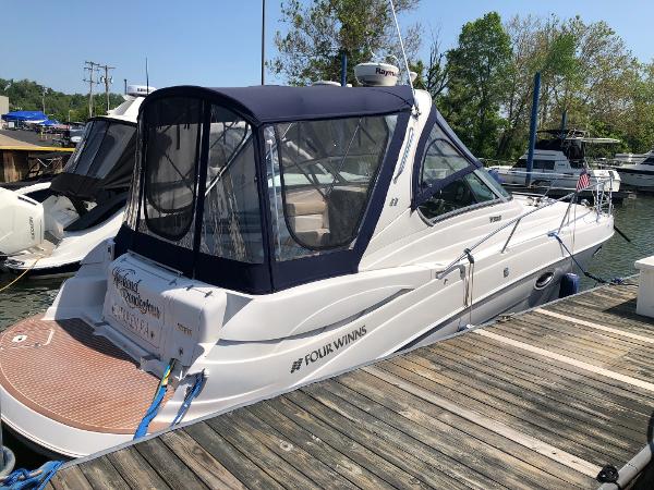 A 2008 Four Winns V338 boat docked at a wooden pier. It features a blue canopy.