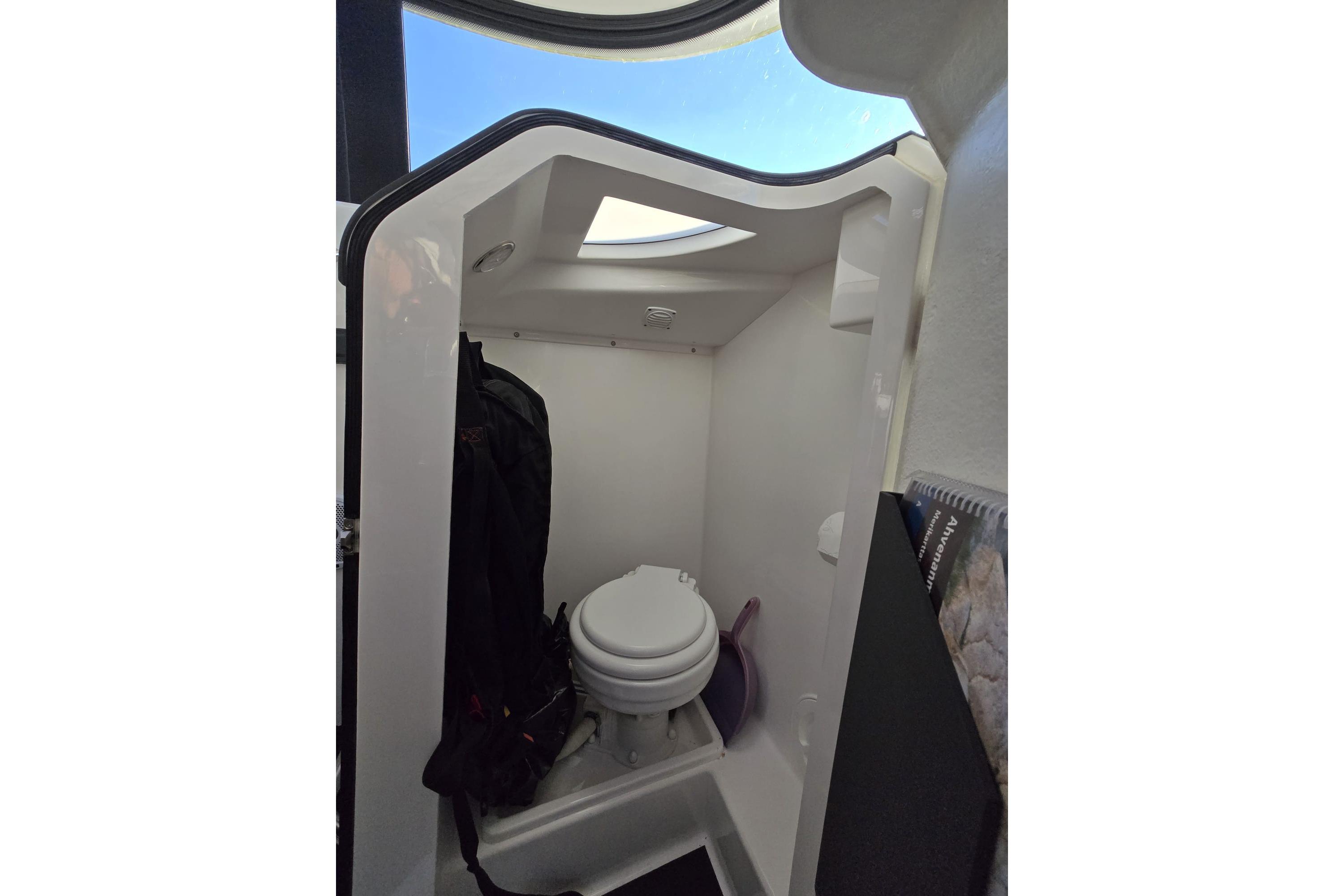 Compact bathroom inside 2016 XO Boats 270 RS, featuring a toilet and storage space.