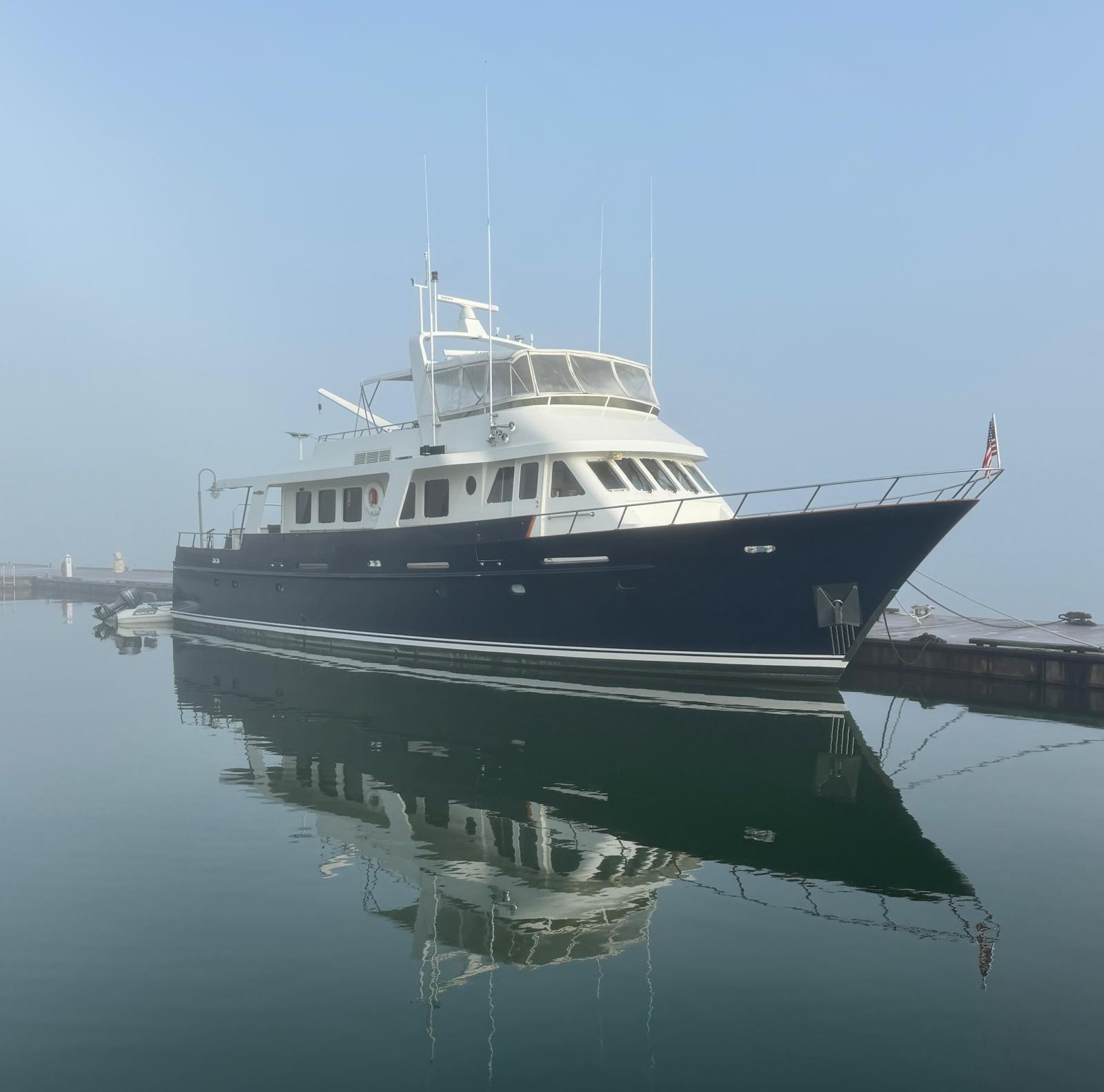 A 1987 Jongert 78 Motor Yacht sits calmly on the water at a dock.
