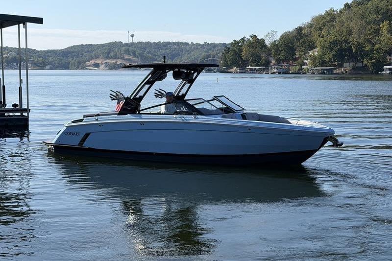 2026 Cobalt R8 Surf boat on a serene lake with wooded shoreline.