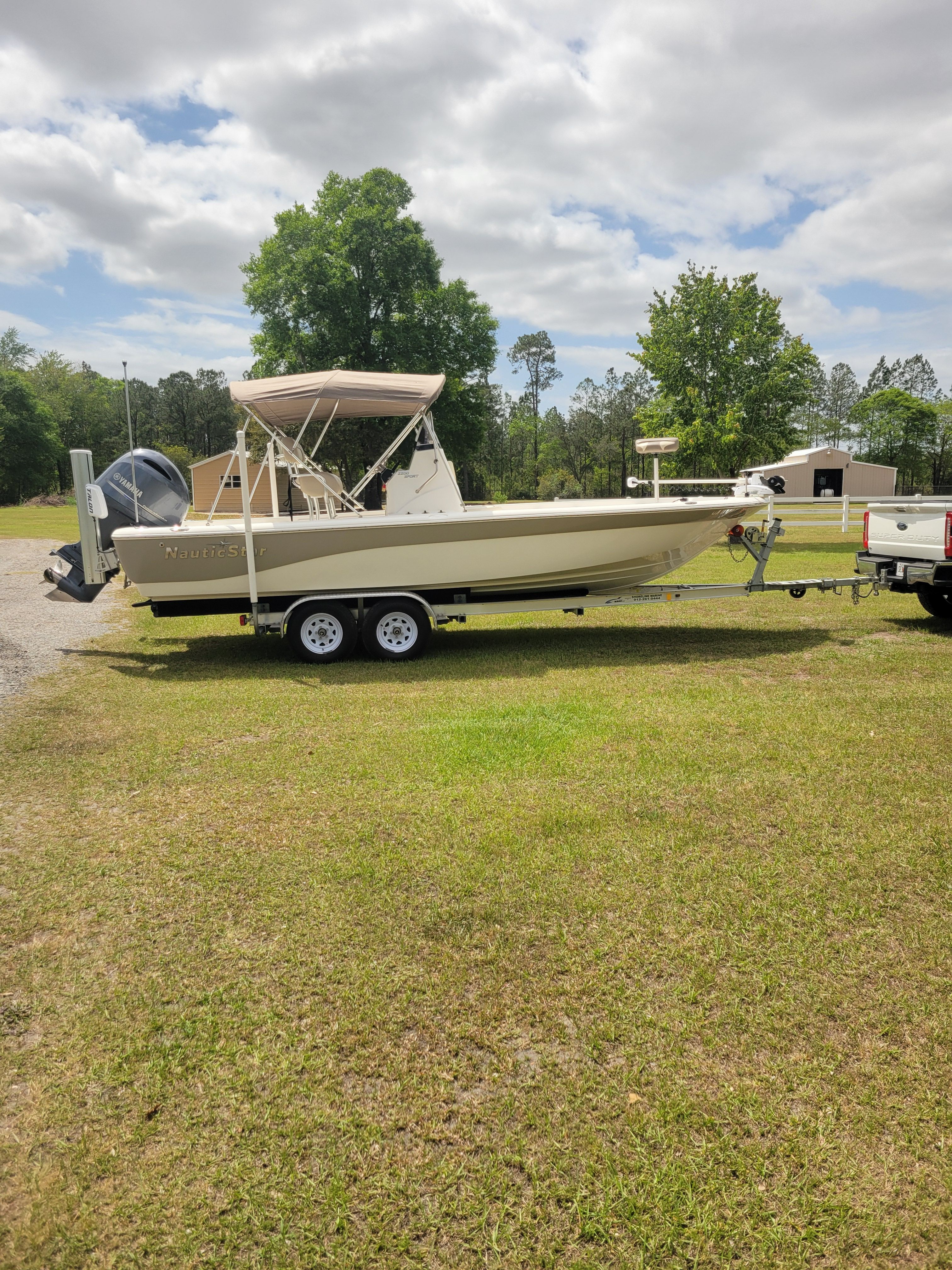 A NauticStar 2200 Sport boat on a trailer on a grassy area.