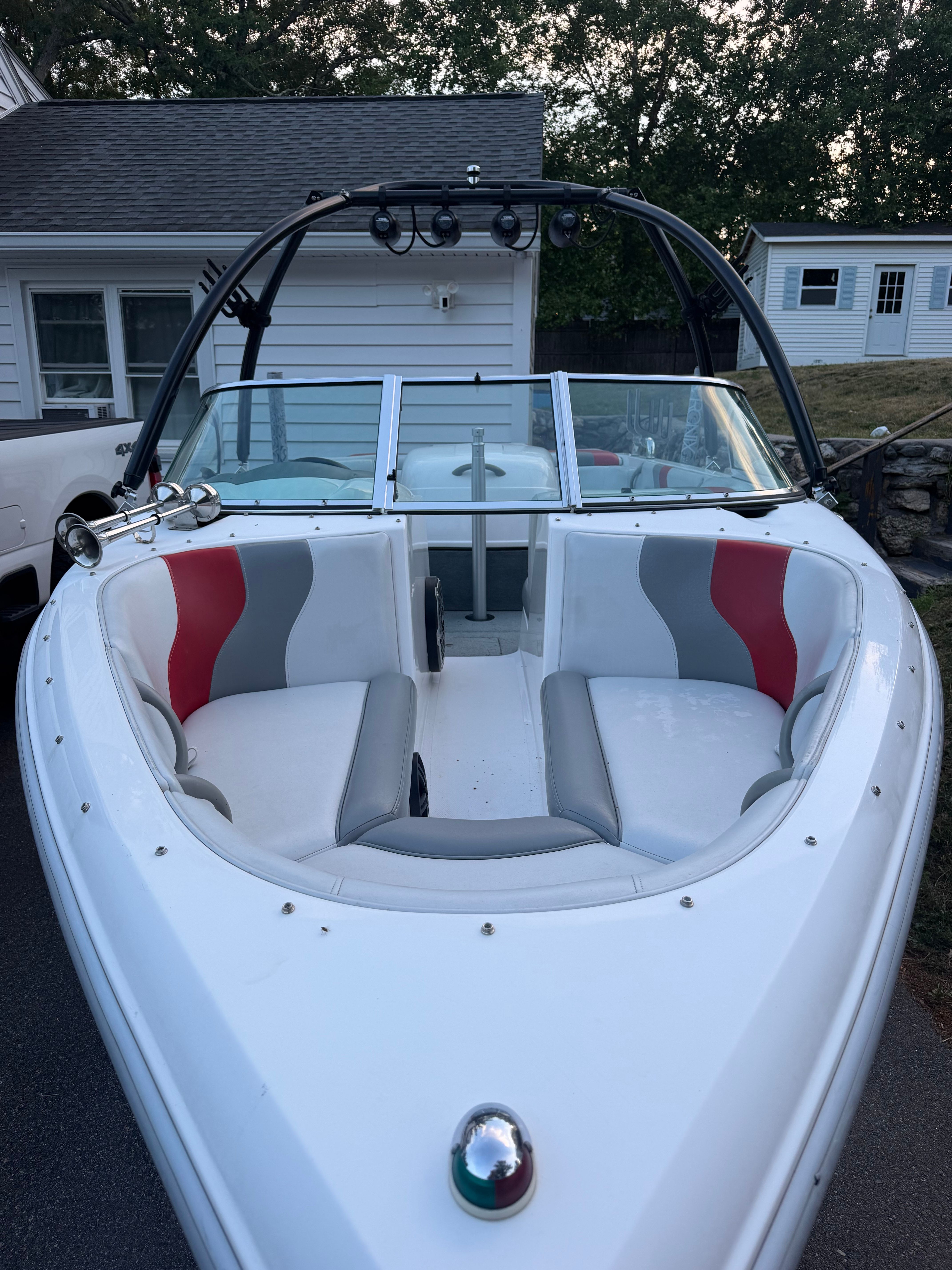 A white motorboat with red and gray seats is on a trailer in front of a house.