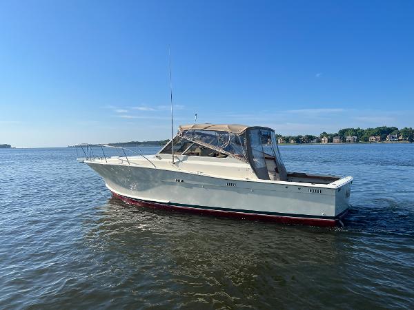 A white boat with a red underside cruises on calm water under a blue sky.