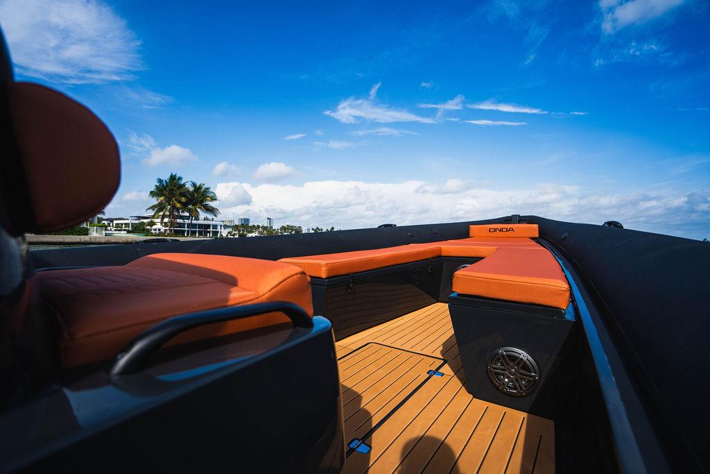 Luxurious 2025 Onda Magna boat with orange seating, wooden deck, and scenic ocean view.