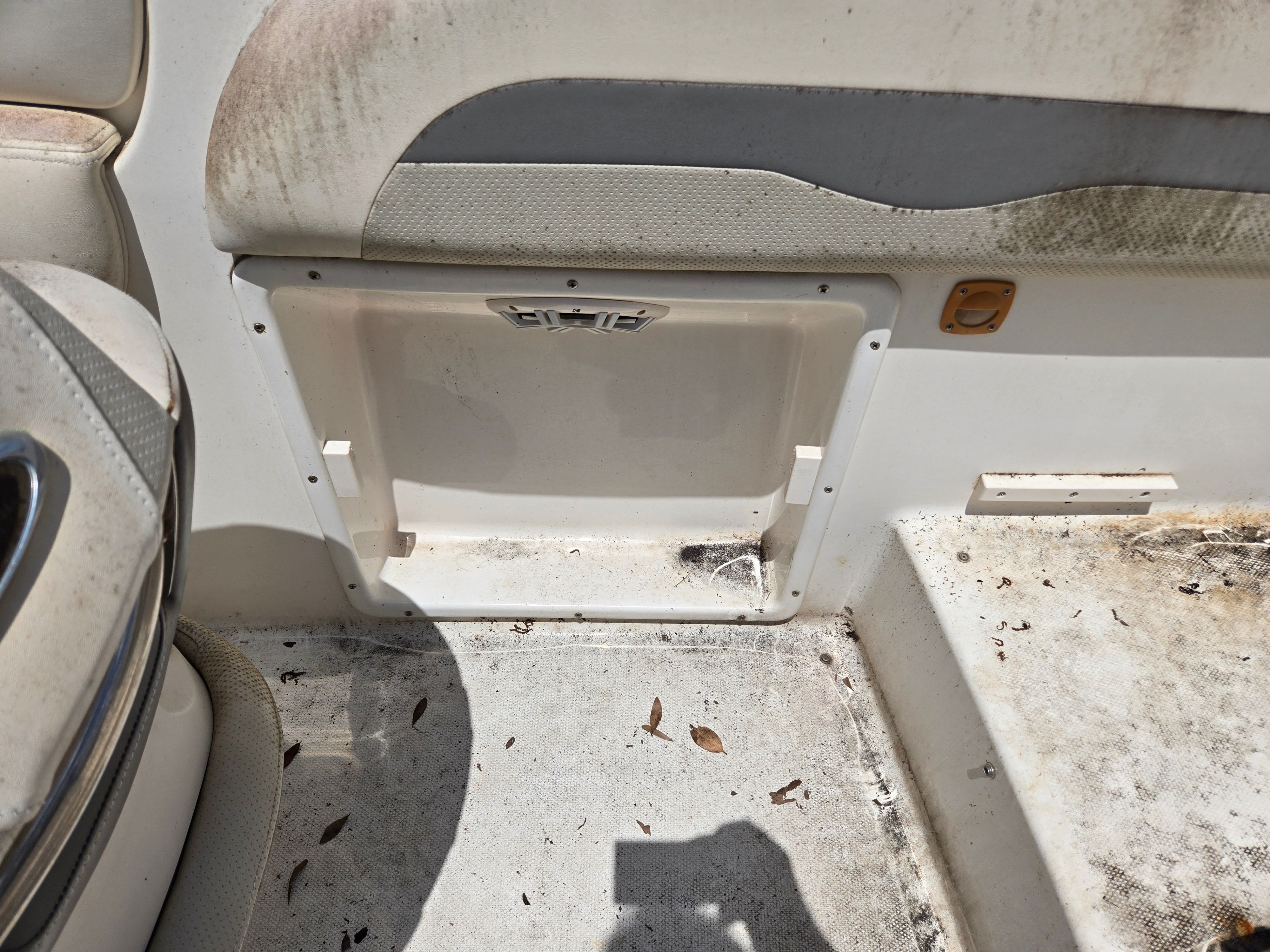 A worn boat seat with dirt and leaves on the floor.