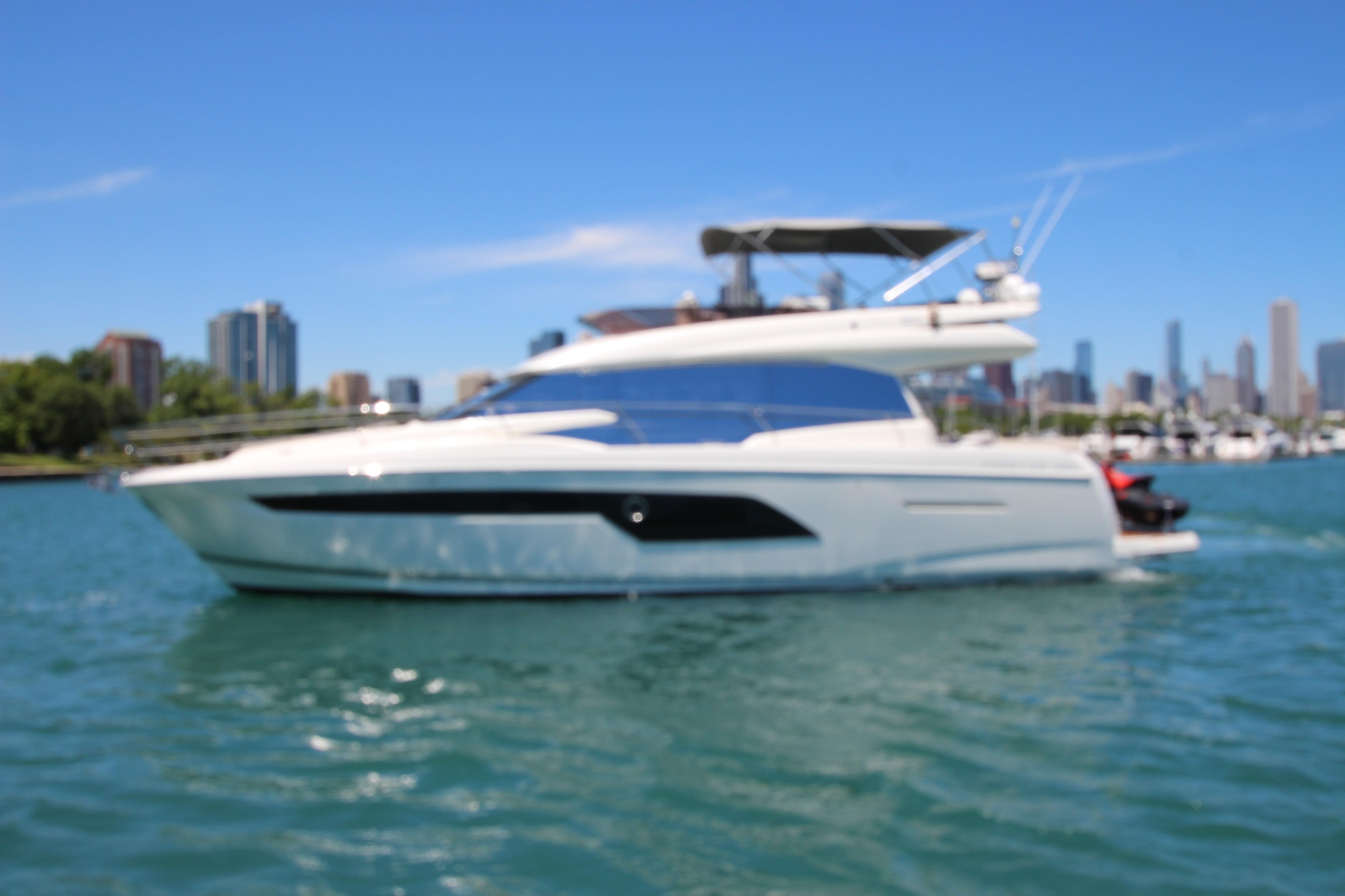 Luxury 2022 Prestige 520 yacht cruising on a sunny day with city skyline backdrop.