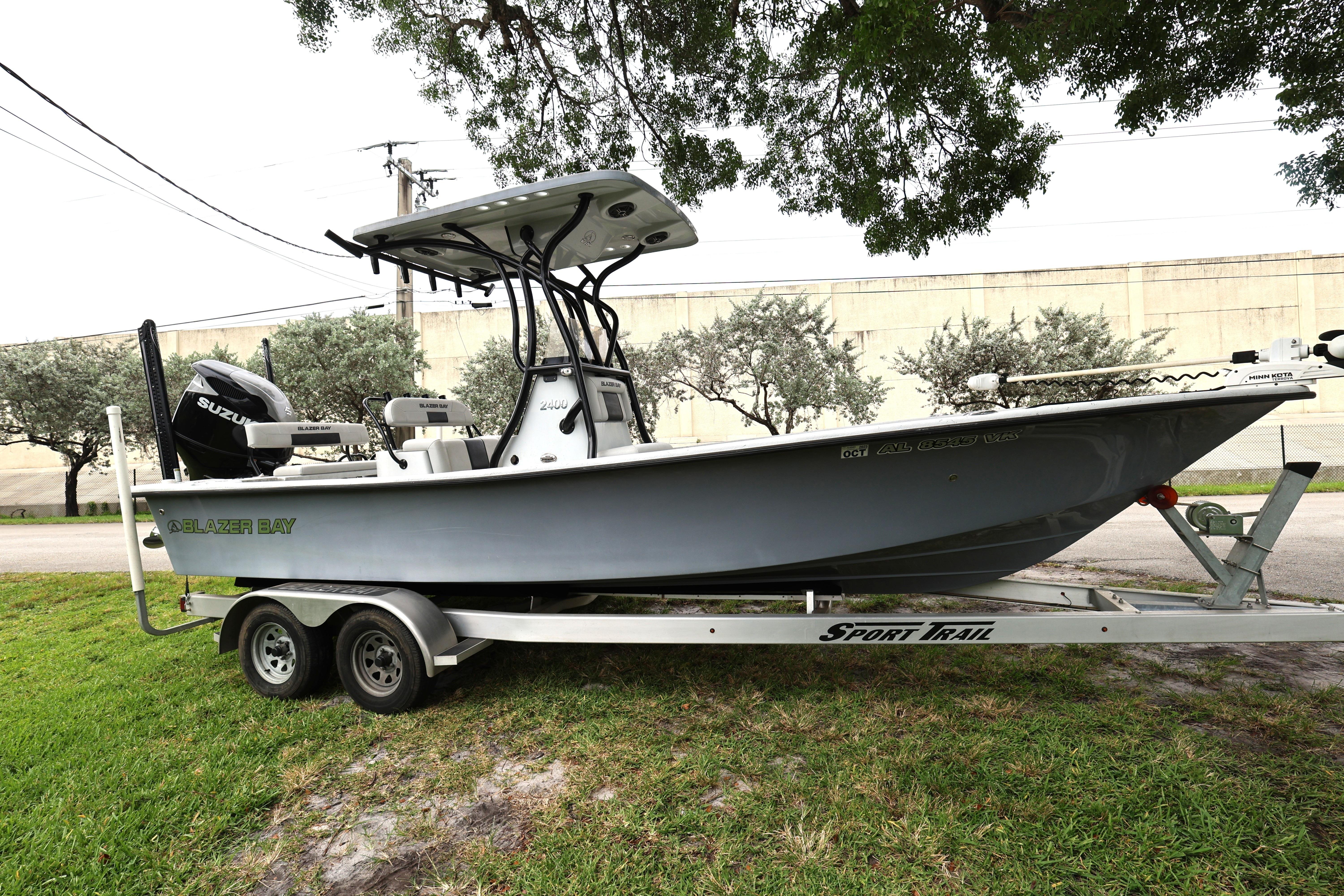 2021 Blazer Bay 2400 boat on trailer, parked outdoors under trees.
