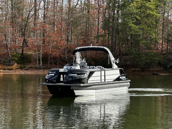 2025 Montara Surf Boss 2.0 25 pontoon boat on a calm lake, surrounded by trees.