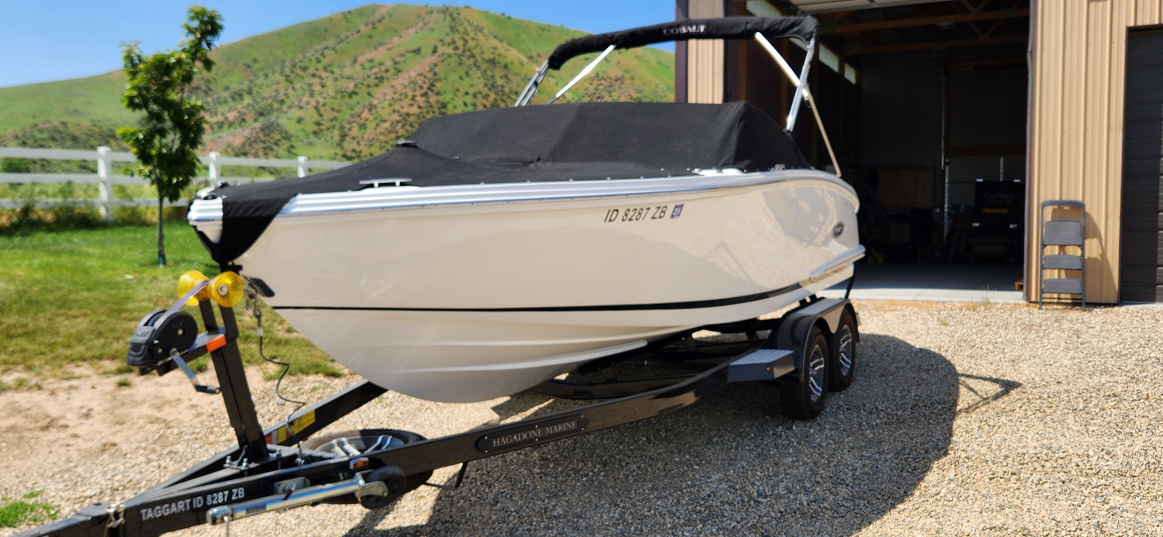 A white Cobalt CS22 boat on a trailer in front of a garage.