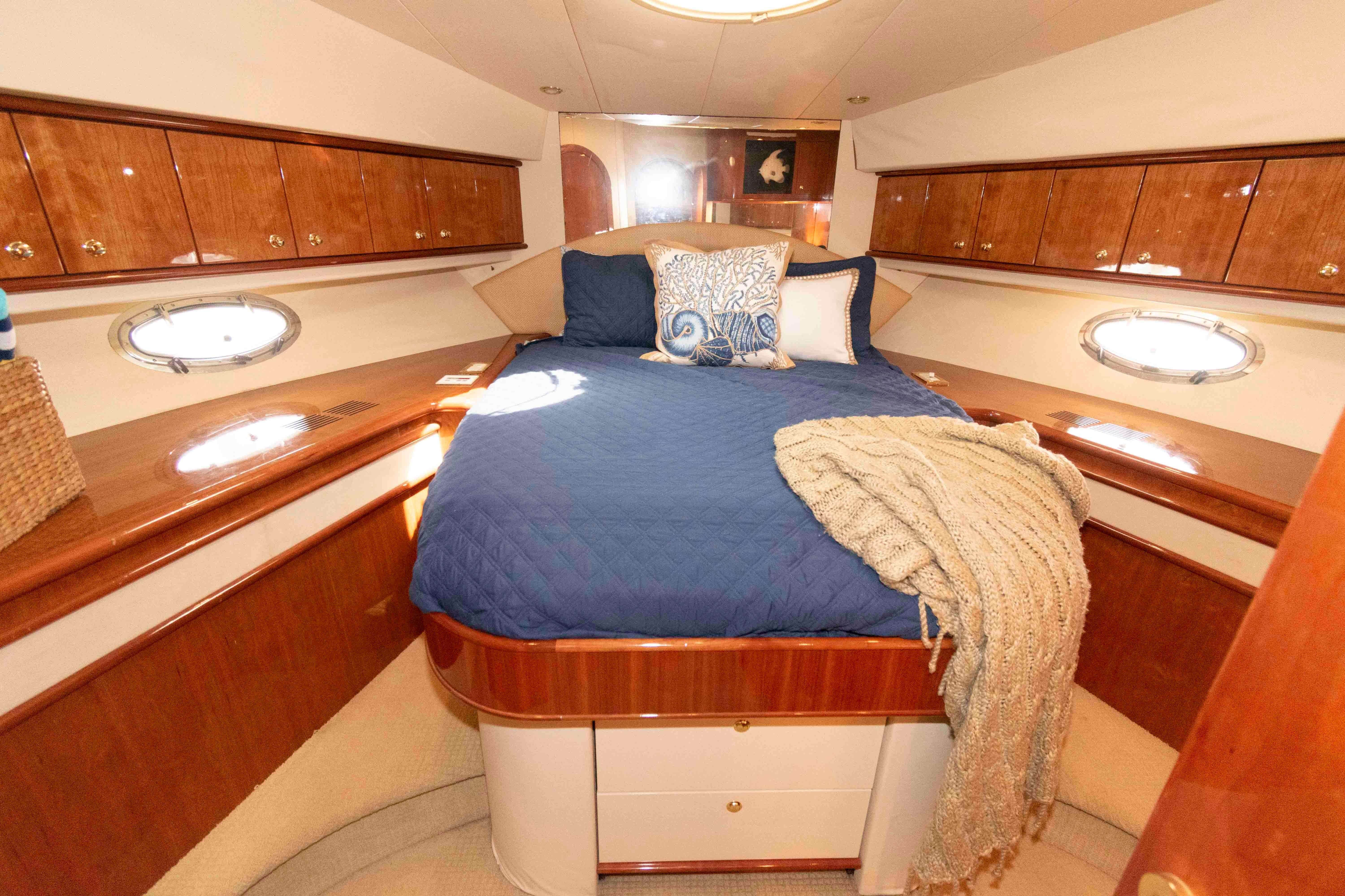 Luxurious 2003 Neptunus 56 Flybridge yacht bedroom with elegant wood cabinetry and cozy bedding.