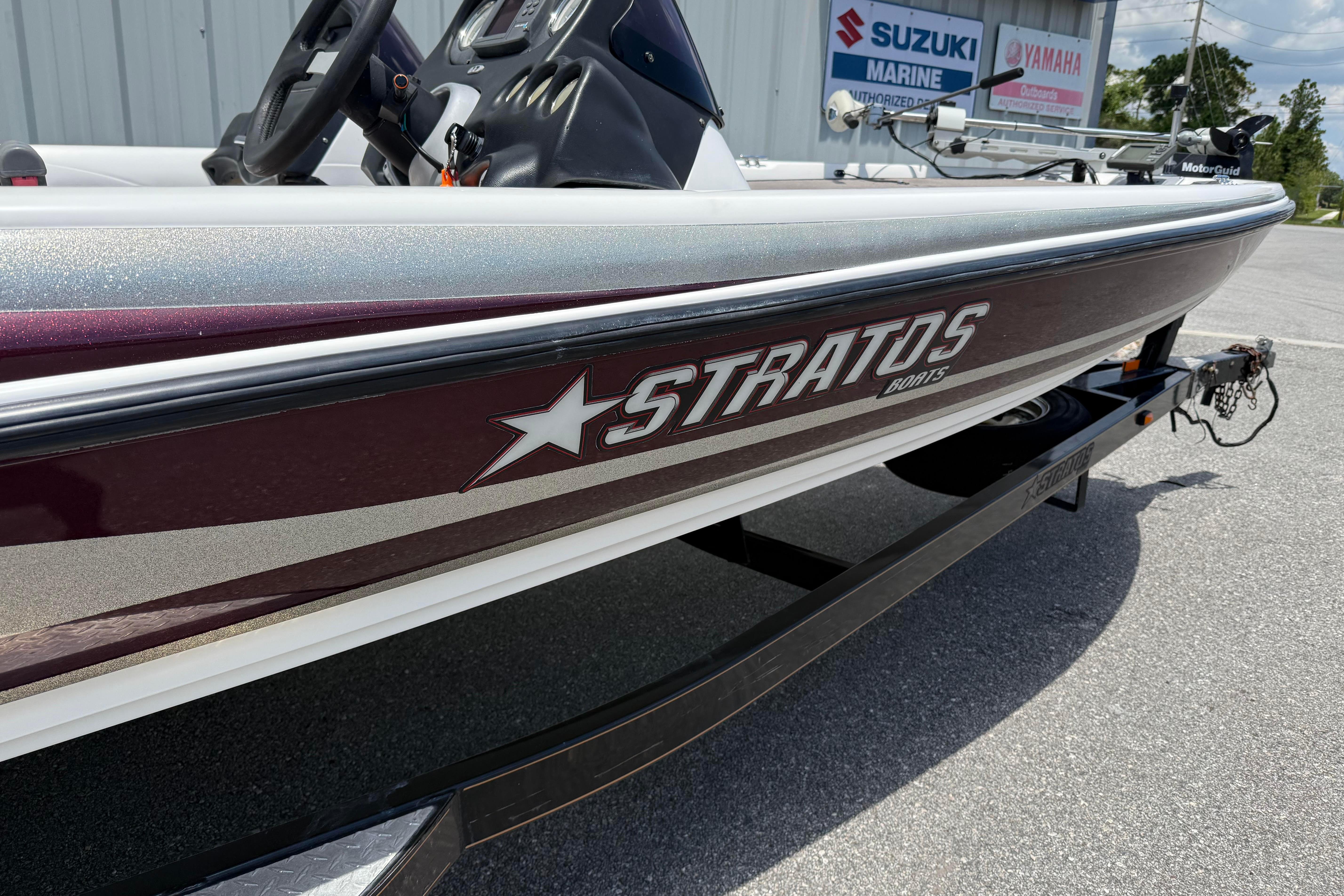 2006 Stratos 294 Pro XL boat with maroon and silver detailing, parked near Suzuki and Yamaha signs.