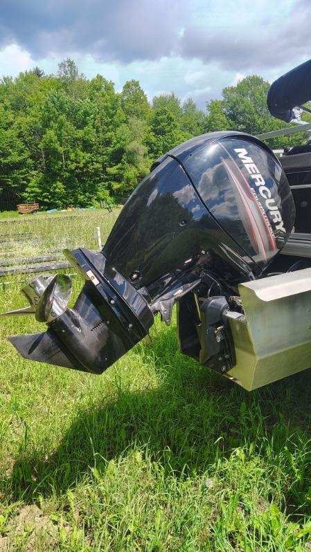 Outboard motor of a boat on grass, surrounded by trees.