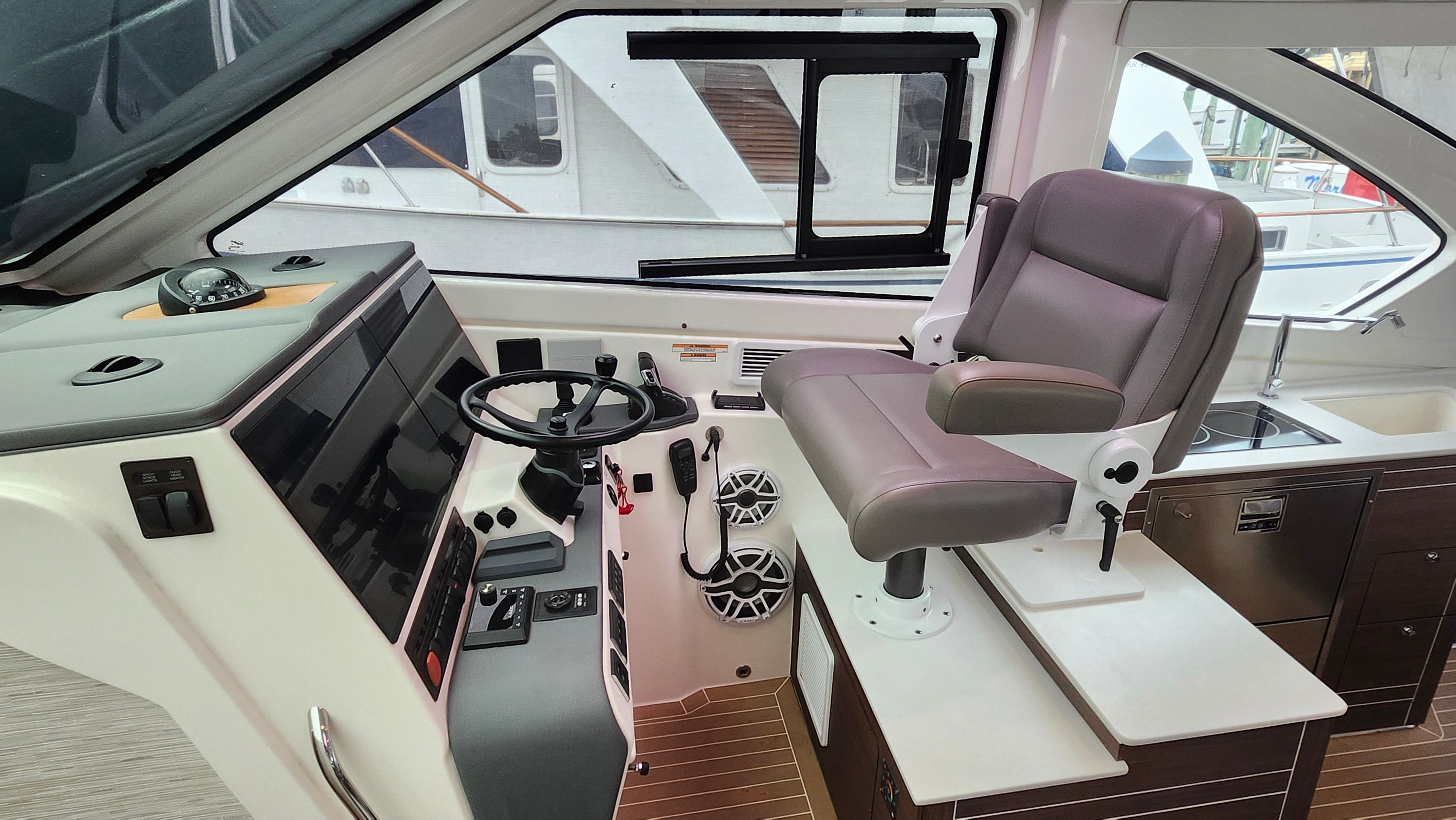 Interior view of a modern boat helm with a cushioned captain's chair and large control panel.