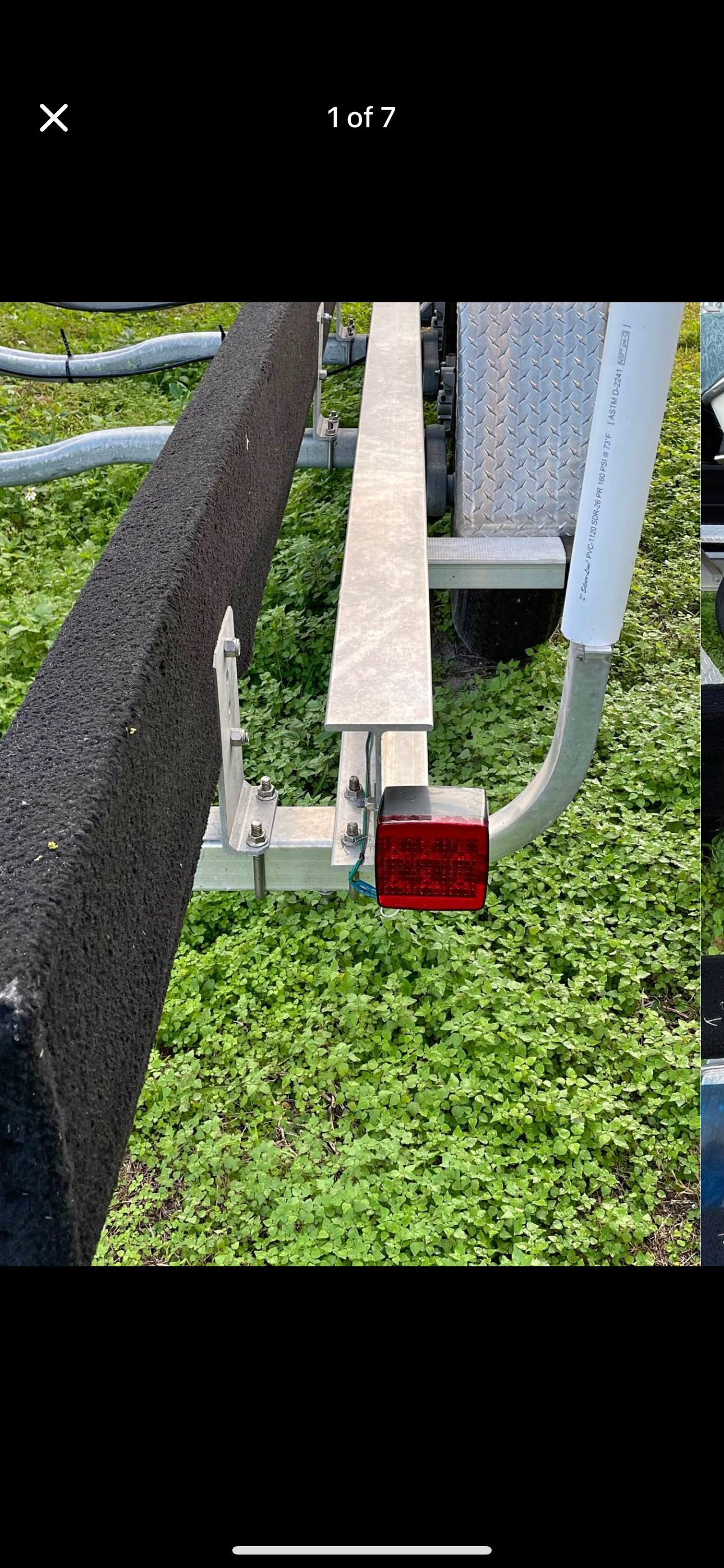 A boat trailer with green vegetation in the background. Visible are metal parts and a red taillight.