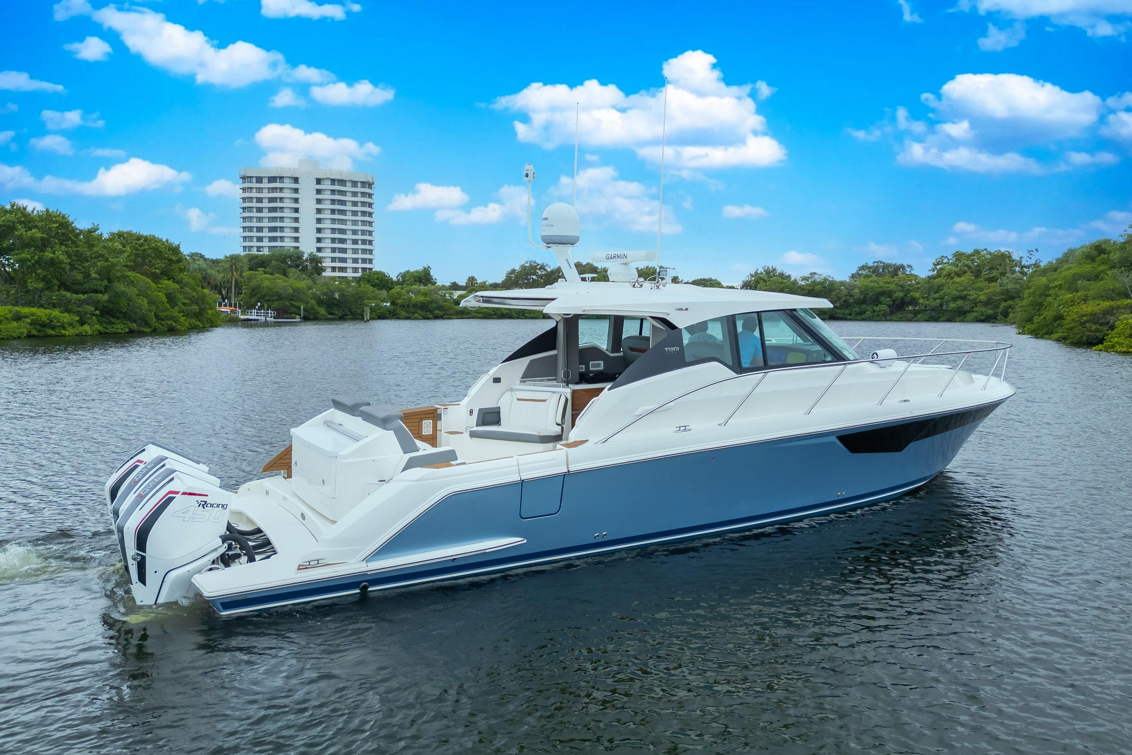 2021 Tiara Sport 43 LE yacht cruising on a scenic river under a blue sky.
