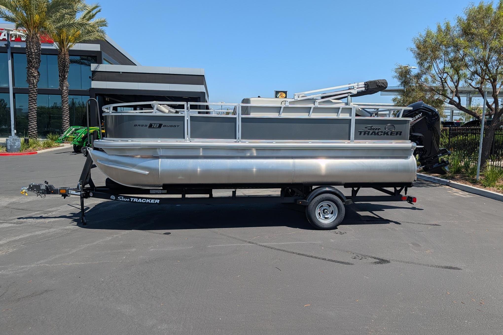 2026 Sun Tracker Bass Buggy 18 DLX pontoon boat on trailer in parking lot.