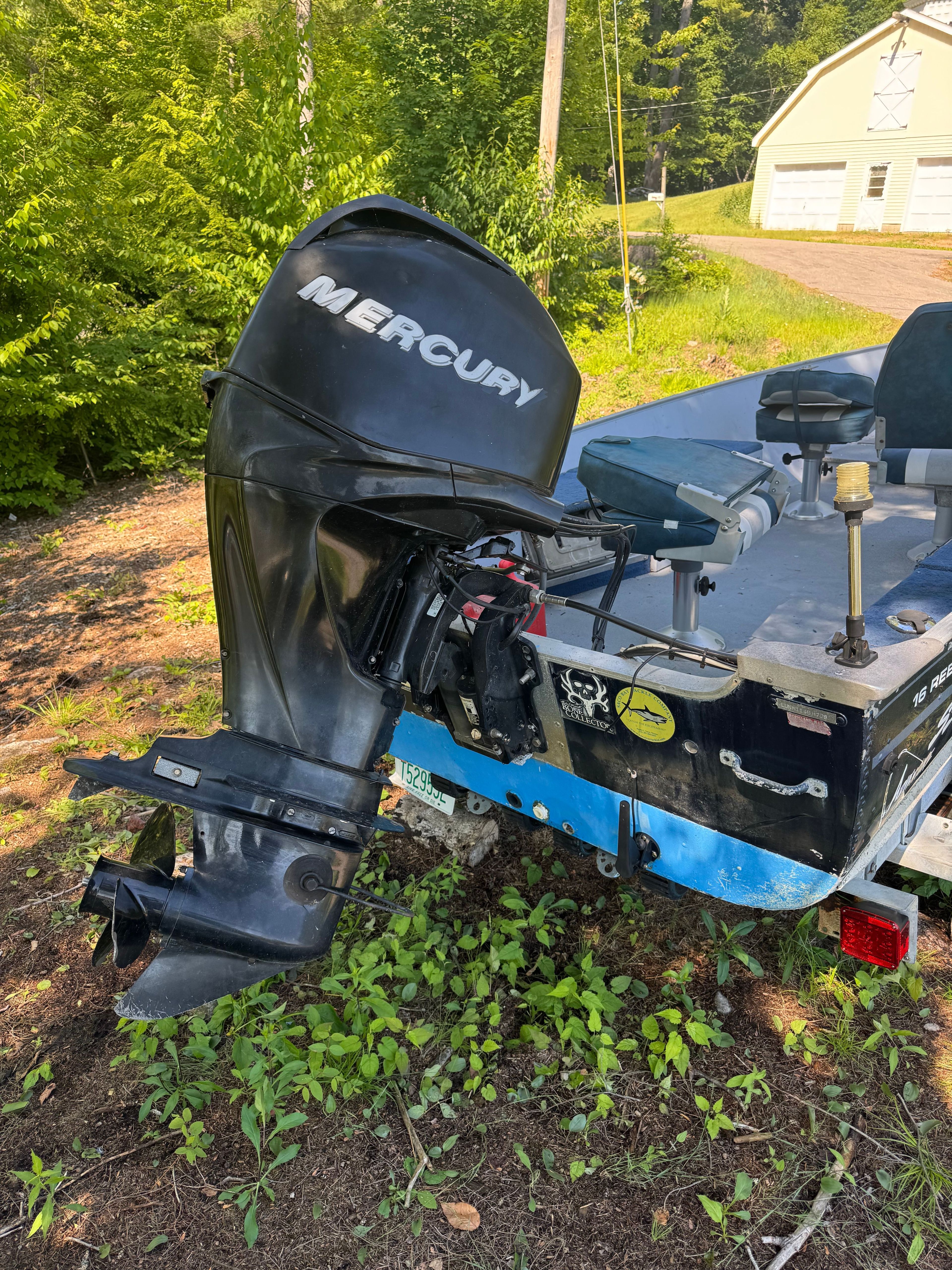 A boat with a Mercury outboard motor is on a trailer in a grassy area.
