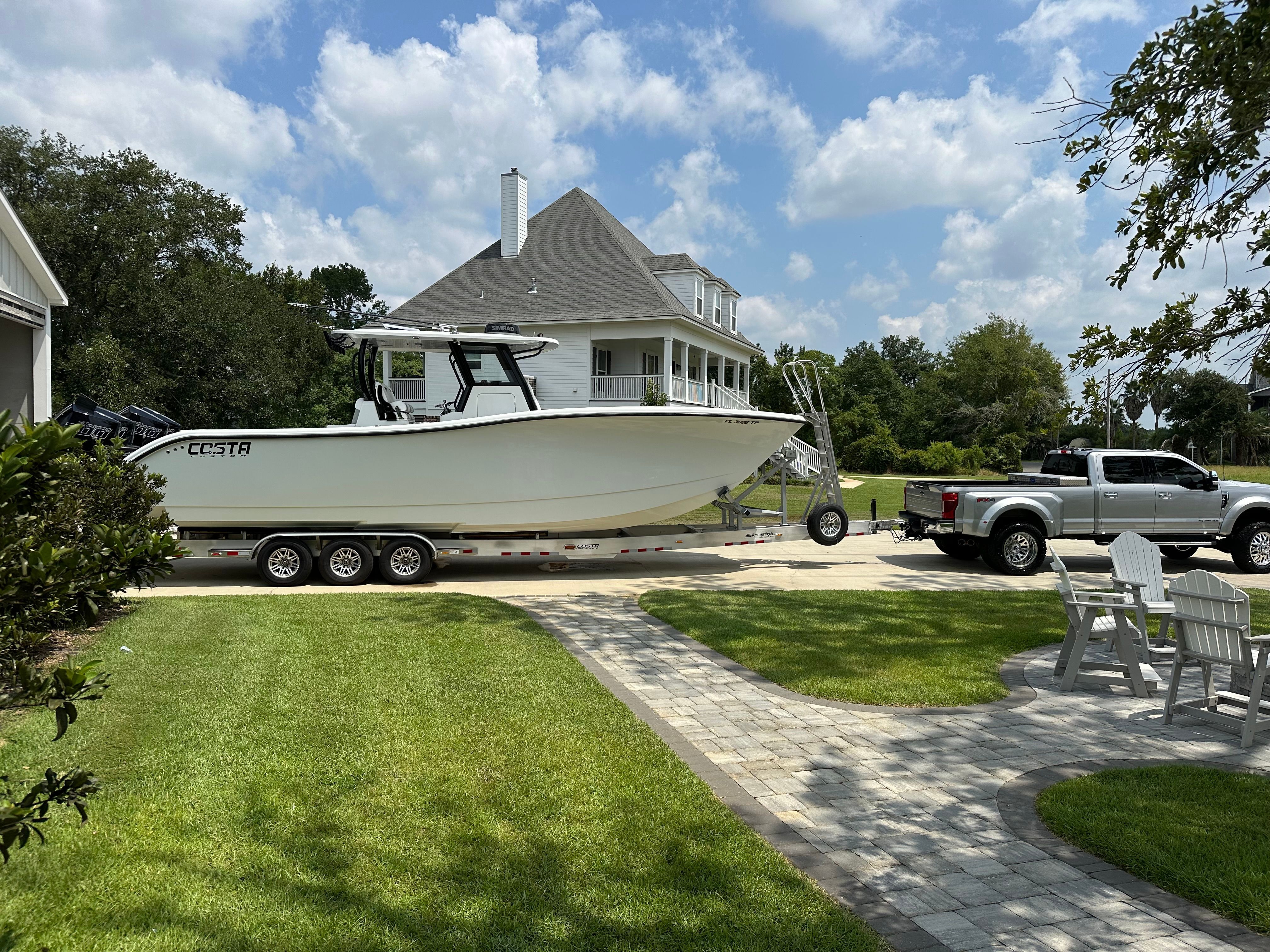 A white boat on a trailer in front of a house with a garden.