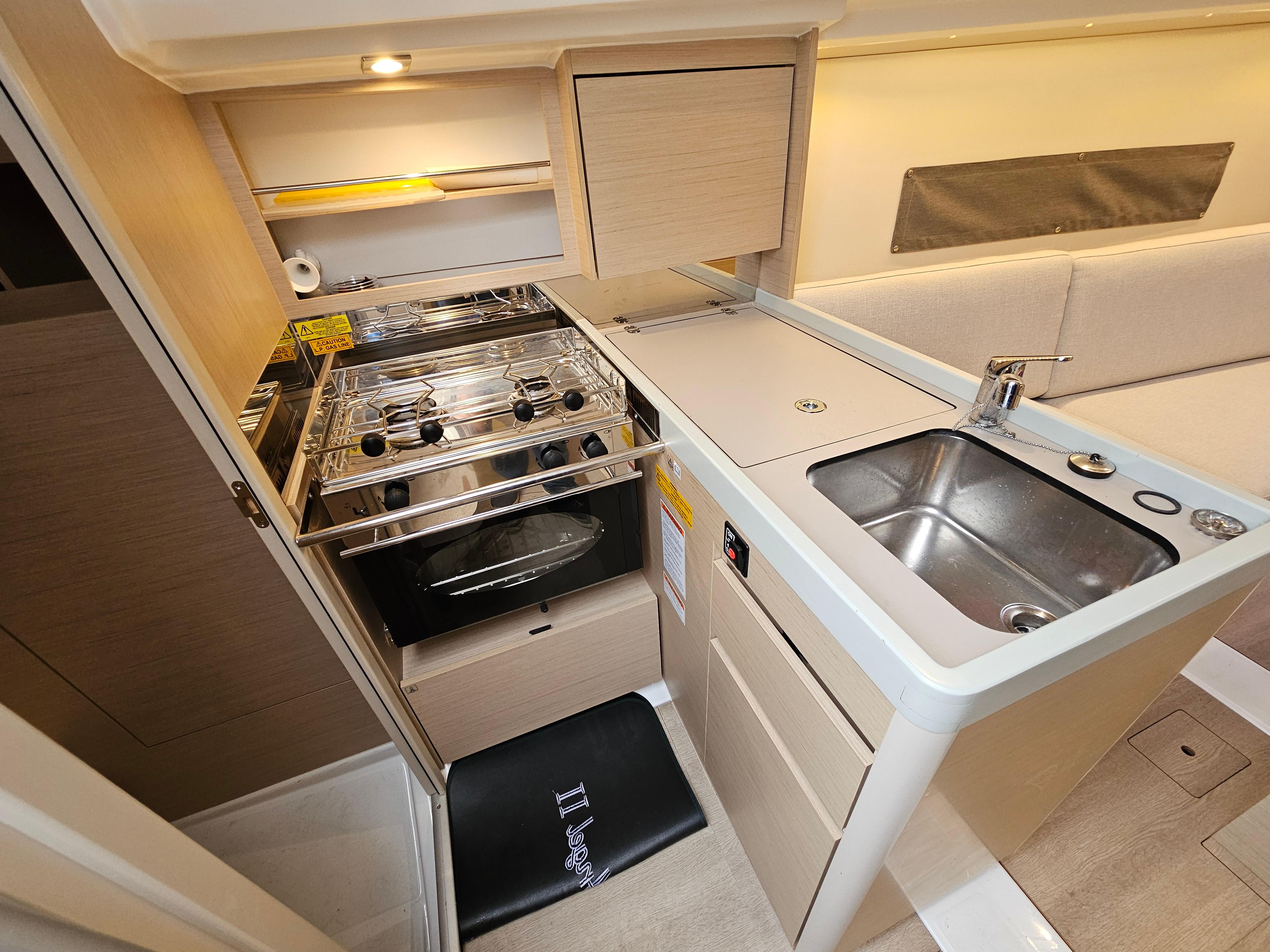 Modern kitchen in 2022 Beneteau Oceanis 30.1 yacht with stove, sink, and storage.