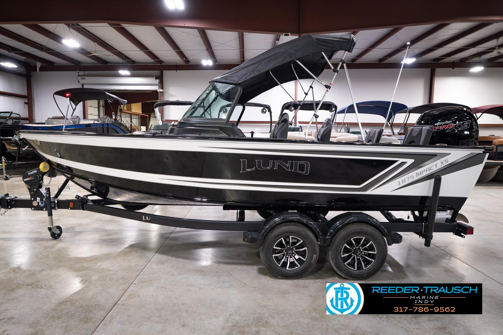 2026 Lund 1875 Impact XS SS boat in showroom, featuring sleek design and dual-axle trailer.