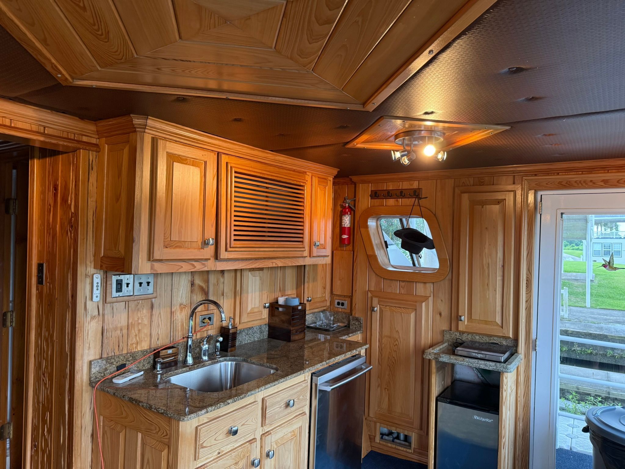 Interior of a luxurious boat kitchen with wood paneling, sink, refrigerator, and window.