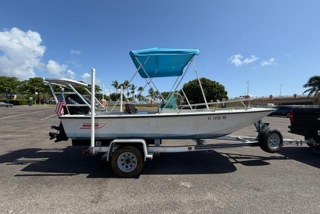 1990 Boston Whaler 17 Newport boat on trailer, blue canopy, parked outdoors.