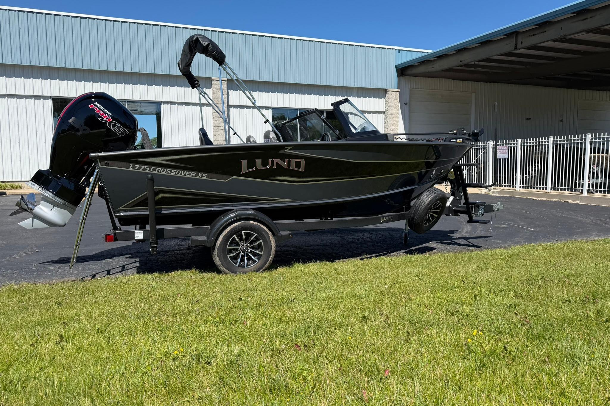 2027 Lund 1775 Crossover XS boat on trailer, parked outdoors near industrial building.