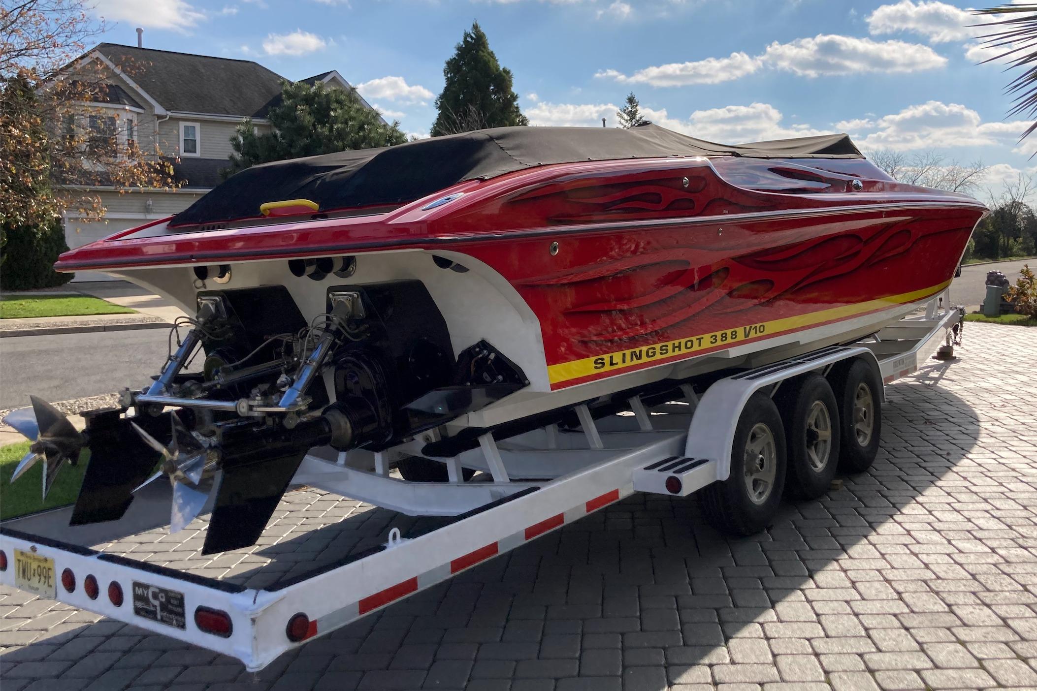 Red 2005 Hustler 388 SLINGSHOT boat on trailer, parked in residential driveway.