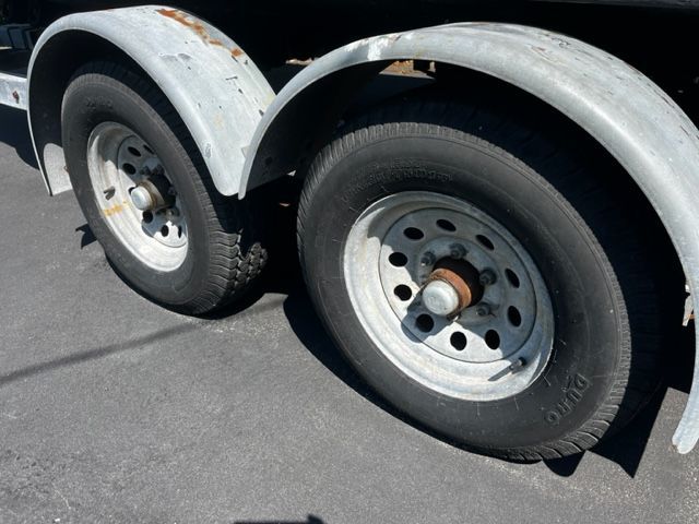 A tandem axle trailer with worn tires and rust spots on the fenders.