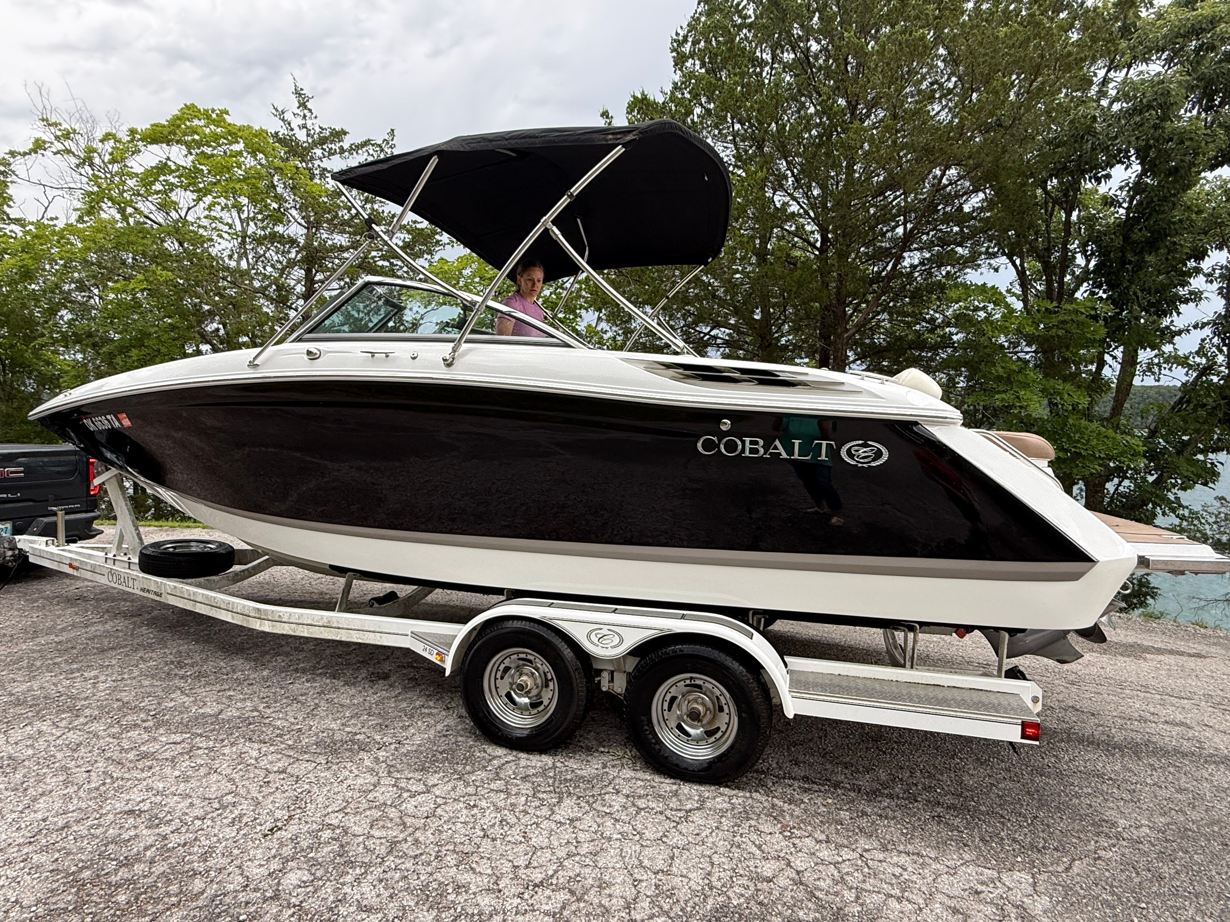 A 2015 Cobalt boat on a trailer, surrounded by trees.