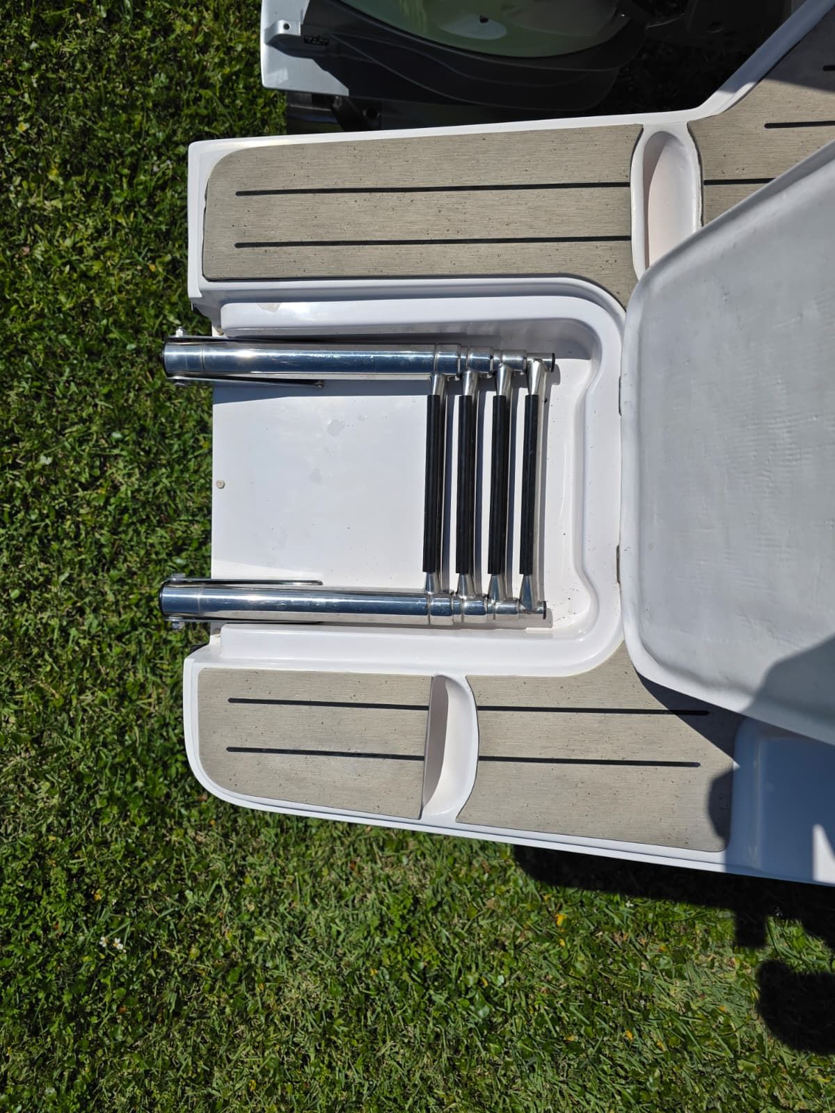 A swim platform with a retractable ladder on a boat, surrounded by green grass.