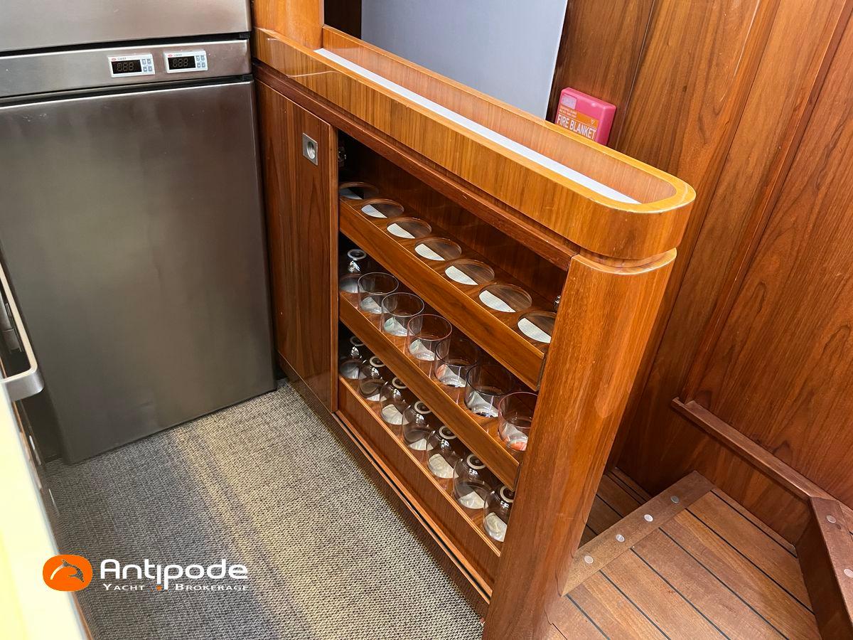 Wooden interior of 2010 Amel 64 yacht with glass storage and stainless steel fridge.