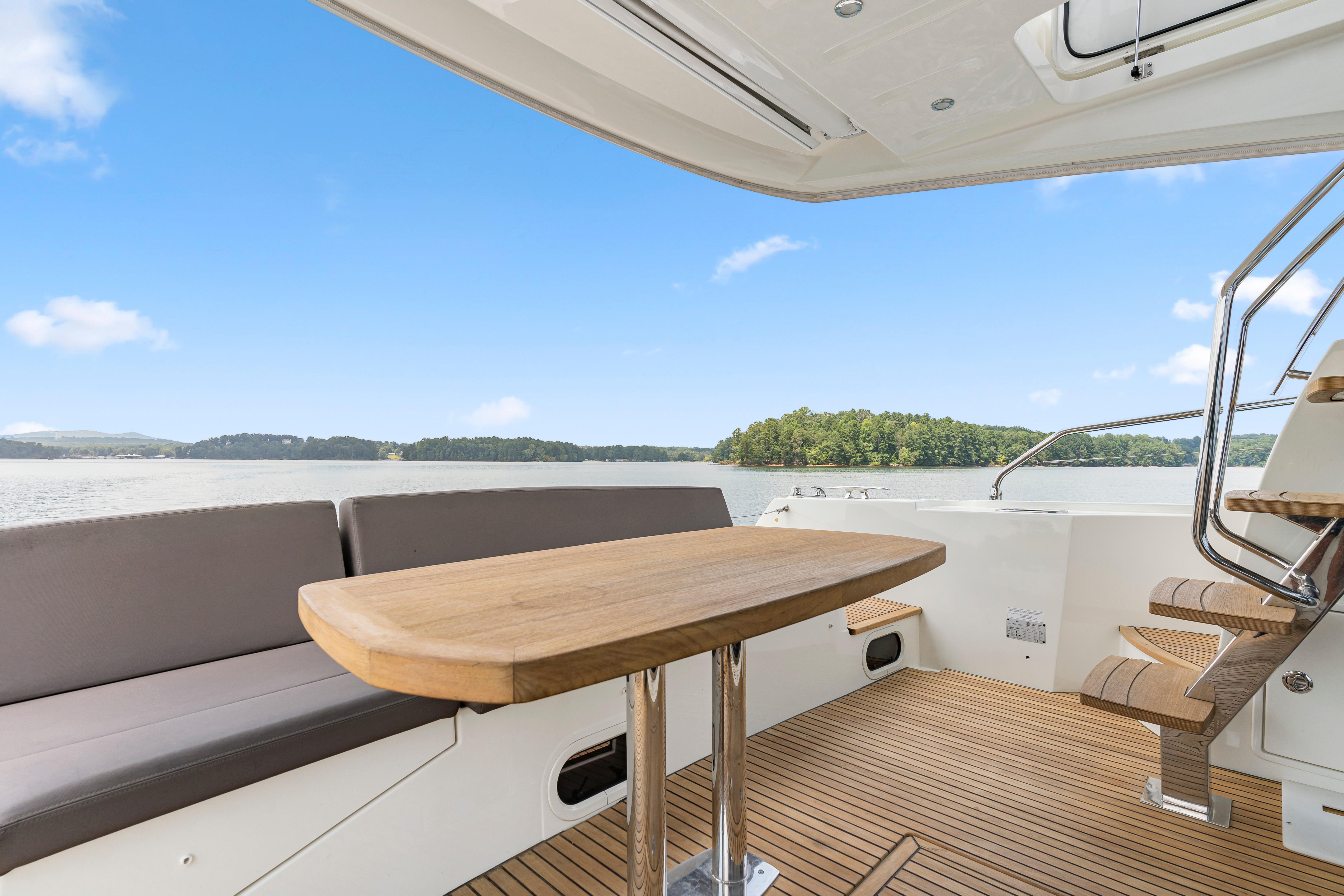 Luxurious 2017 Prestige 500 yacht deck with seating, wooden table, and scenic water view.