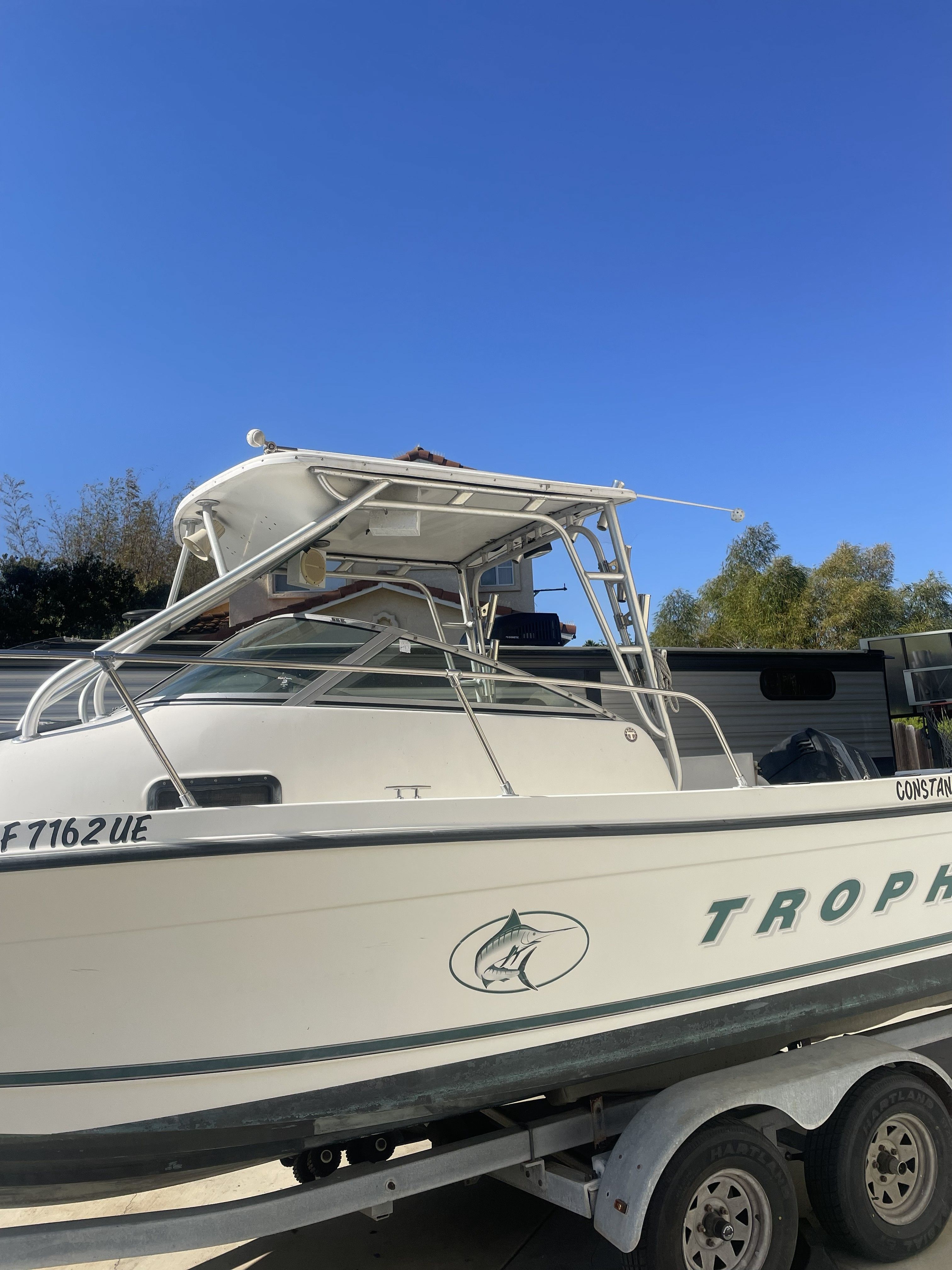 A Bayliner Trophy boat on a trailer, surrounded by trees and a clear blue sky.
